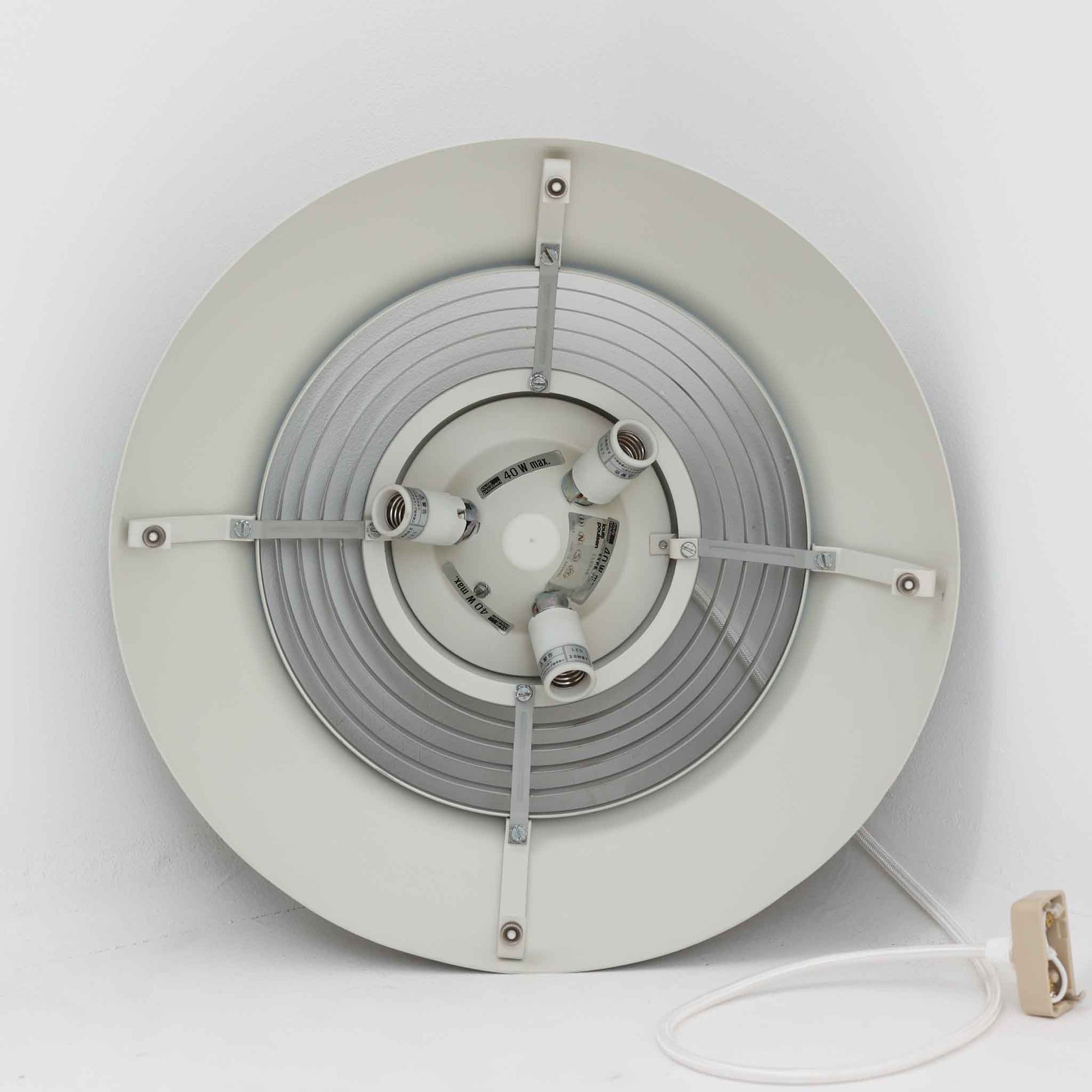 Arne JacobsenがLouis Poulsenのためにデザインした「AJ Royal 370」ペンダントライトです。直径37cmのサイズで、段階的に重なる上部シェードと、下面を覆うアクリルディフューザーによって光が柔らかく拡散し、均一で心地よい明かりを提供します。アルミとスチールの堅牢な構造に加え、シンプルかつモダンなフォルムが空間に洗練された印象を与えます。ダイニングやリビングに適した存在感ある照明で、北欧デザインを象徴するビンテージアイテムです。現行モデルでは展開されていないライトグレーのカラーは、当時のオリジナル品ならではの希少な仕様であり、コレクターズアイテムとしても高い価値を持っています。