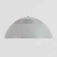 Arne JacobsenがLouis Poulsenのためにデザインした「AJ Royal 370」ペンダントライトです。直径37cmのサイズで、段階的に重なる上部シェードと、下面を覆うアクリルディフューザーによって光が柔らかく拡散し、均一で心地よい明かりを提供します。アルミとスチールの堅牢な構造に加え、シンプルかつモダンなフォルムが空間に洗練された印象を与えます。ダイニングやリビングに適した存在感ある照明で、北欧デザインを象徴するビンテージアイテムです。現行モデルでは展開されていないライトグレーのカラーは、当時のオリジナル品ならではの希少な仕様であり、コレクターズアイテムとしても高い価値を持っています。