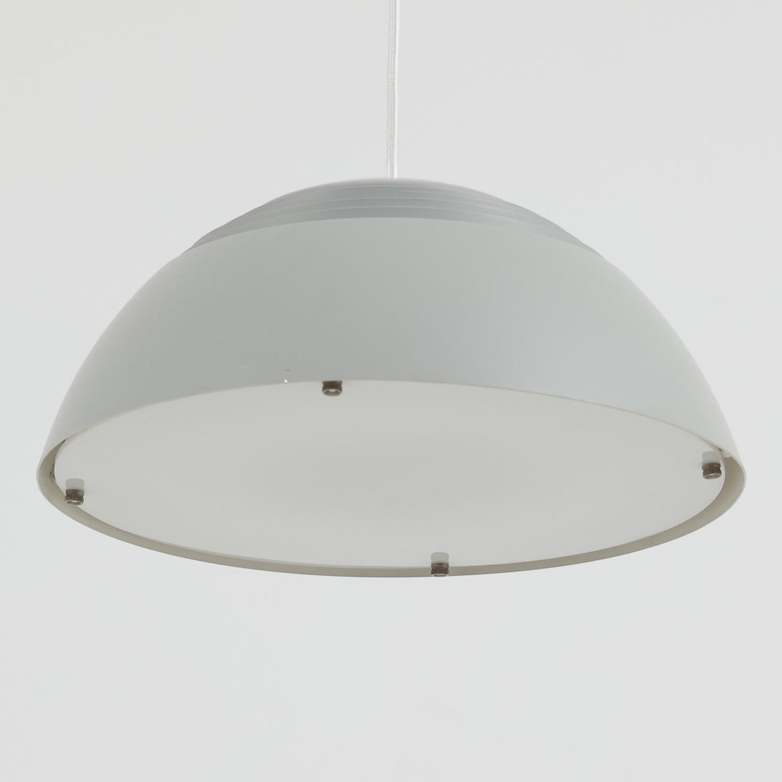Arne JacobsenがLouis Poulsenのためにデザインした「AJ Royal 370」ペンダントライトです。直径37cmのサイズで、段階的に重なる上部シェードと、下面を覆うアクリルディフューザーによって光が柔らかく拡散し、均一で心地よい明かりを提供します。アルミとスチールの堅牢な構造に加え、シンプルかつモダンなフォルムが空間に洗練された印象を与えます。ダイニングやリビングに適した存在感ある照明で、北欧デザインを象徴するビンテージアイテムです。現行モデルでは展開されていないライトグレーのカラーは、当時のオリジナル品ならではの希少な仕様であり、コレクターズアイテムとしても高い価値を持っています。