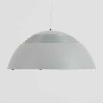 Arne JacobsenがLouis Poulsenのためにデザインした「AJ Royal 370」ペンダントライトです。直径37cmのサイズで、段階的に重なる上部シェードと、下面を覆うアクリルディフューザーによって光が柔らかく拡散し、均一で心地よい明かりを提供します。アルミとスチールの堅牢な構造に加え、シンプルかつモダンなフォルムが空間に洗練された印象を与えます。ダイニングやリビングに適した存在感ある照明で、北欧デザインを象徴するビンテージアイテムです。現行モデルでは展開されていないライトグレーのカラーは、当時のオリジナル品ならではの希少な仕様であり、コレクターズアイテムとしても高い価値を持っています。