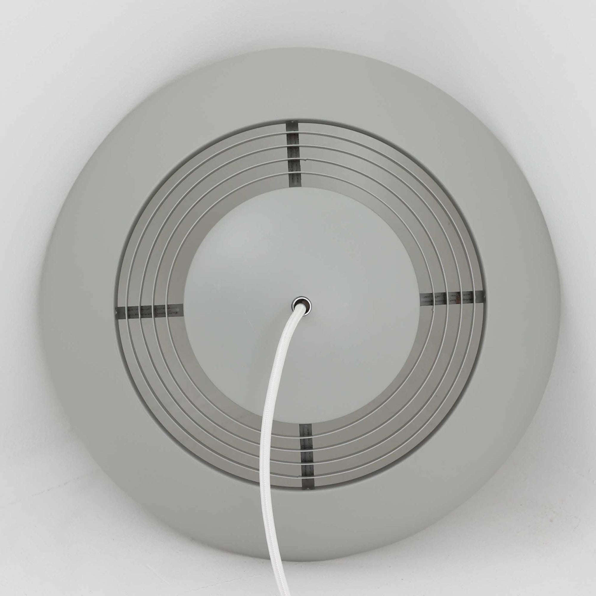 Arne JacobsenがLouis Poulsenのためにデザインした「AJ Royal 370」ペンダントライトです。直径37cmのサイズで、段階的に重なる上部シェードと、下面を覆うアクリルディフューザーによって光が柔らかく拡散し、均一で心地よい明かりを提供します。アルミとスチールの堅牢な構造に加え、シンプルかつモダンなフォルムが空間に洗練された印象を与えます。ダイニングやリビングに適した存在感ある照明で、北欧デザインを象徴するビンテージアイテムです。現行モデルでは展開されていないライトグレーのカラーは、当時のオリジナル品ならではの希少な仕様であり、コレクターズアイテムとしても高い価値を持っています。