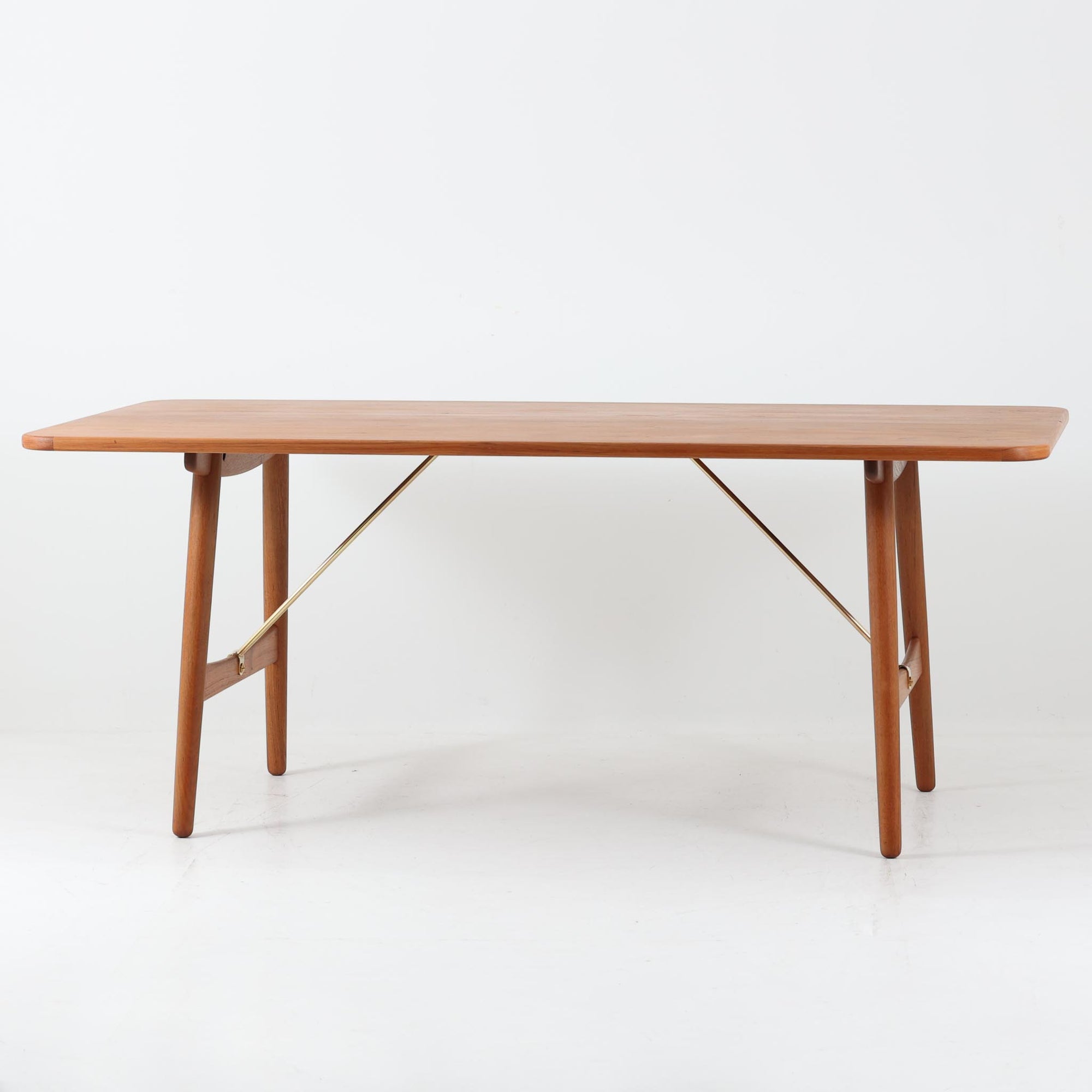 Borge Mogensenがデザインし、Soborg Mobler社より製造されたダイニングテーブル「BM1160」ハンティングテーブルです。現行品はカール・ハンセン社からも展開されていますが、こちらはSoborg社製造によるビンテージ品で、現在では入手が難しいチーク材仕様となっています。幅180cmと現行品よりややコンパクトなサイズ感で、日本の住空間にも取り入れやすい設計です。豊かな木目を持つチーク材の天板に、脚部を支える真鍮製クロスバーを組み合わせることで、堅牢さと美しさを兼ね備えています。角には滑らかな曲線が施され、温かみのある印象を添えつつ、家族や来客を迎える食卓として十分な広さを誇ります。真鍮パーツは構造的強度を高めると同時にビンテージらしい上質なアクセントとなり、シンプルでありながら存在感ある佇まいを演出。北欧家具ならではの実用性とデザイン性が息づき、年月を重ねることでさらに素材の風合いが深まり、空間を豊かに彩ります。