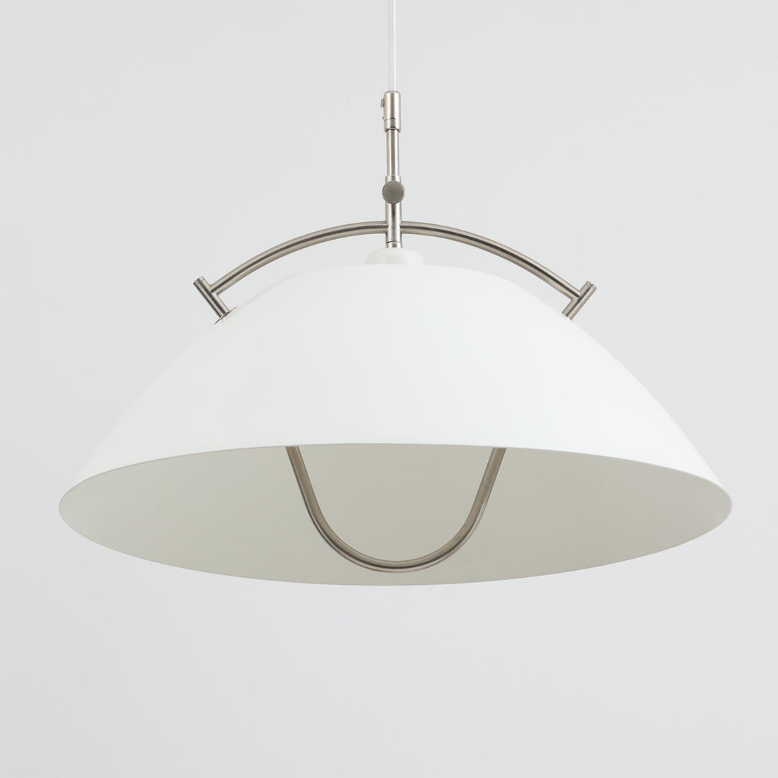 Pandul（パンドゥル）社が正規製造している、ハンス・J・ウェグナー（Hans J. Wegner）デザインのペンダントライト「JH604」です。1960年代にLouis Poulsen（ルイスポールセン）社で製造されていたモデルで、ウェグナーが自邸のためにデザインしたことでも知られています。直径50cmの存在感あるフォルムと、アルミ製シェードとステンレス製アームによる軽やかで堅牢な構造は、北欧デザインらしい機能美を体現。点灯時には下方向だけでなくシェード上部の隙間からも光が柔らかく漏れ、空間に奥行きを与えます。Pandulは1982年にデンマークで設立され、Louis Poulsenから受け継いだ名作を当時のデザインと品質を尊重して製造しているブランドです。なお、本品はプラスチック製コードリールが欠品しておりますが、全体として良好なコンディションを保っています。ヴィンテージデザインの魅力と現行製造ならではの安心感を兼ね備えた、北欧デザインを象徴する一灯です。
