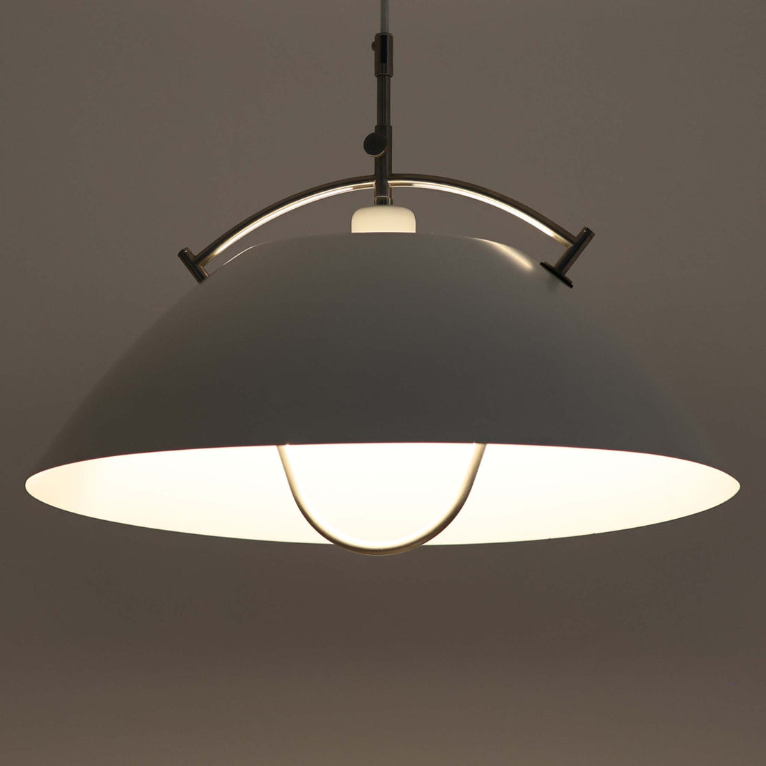 Pandul（パンドゥル）社が正規製造している、ハンス・J・ウェグナー（Hans J. Wegner）デザインのペンダントライト「JH604」です。1960年代にLouis Poulsen（ルイスポールセン）社で製造されていたモデルで、ウェグナーが自邸のためにデザインしたことでも知られています。直径50cmの存在感あるフォルムと、アルミ製シェードとステンレス製アームによる軽やかで堅牢な構造は、北欧デザインらしい機能美を体現。点灯時には下方向だけでなくシェード上部の隙間からも光が柔らかく漏れ、空間に奥行きを与えます。Pandulは1982年にデンマークで設立され、Louis Poulsenから受け継いだ名作を当時のデザインと品質を尊重して製造しているブランドです。なお、本品はプラスチック製コードリールが欠品しておりますが、全体として良好なコンディションを保っています。ヴィンテージデザインの魅力と現行製造ならではの安心感を兼ね備えた、北欧デザインを象徴する一灯です。