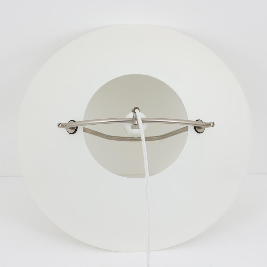 Pandul（パンドゥル）社が正規製造している、ハンス・J・ウェグナー（Hans J. Wegner）デザインのペンダントライト「JH604」です。1960年代にLouis Poulsen（ルイスポールセン）社で製造されていたモデルで、ウェグナーが自邸のためにデザインしたことでも知られています。直径50cmの存在感あるフォルムと、アルミ製シェードとステンレス製アームによる軽やかで堅牢な構造は、北欧デザインらしい機能美を体現。点灯時には下方向だけでなくシェード上部の隙間からも光が柔らかく漏れ、空間に奥行きを与えます。Pandulは1982年にデンマークで設立され、Louis Poulsenから受け継いだ名作を当時のデザインと品質を尊重して製造しているブランドです。なお、本品はプラスチック製コードリールが欠品しておりますが、全体として良好なコンディションを保っています。ヴィンテージデザインの魅力と現行製造ならではの安心感を兼ね備えた、北欧デザインを象徴する一灯です。