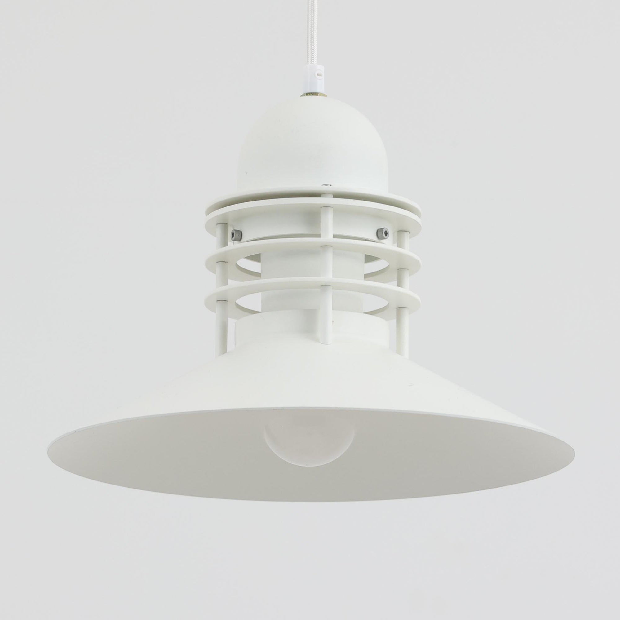 Alfred HomannとOle V. Kjaerによってデザインされ、Louis Poulsen社から製造されたペンダントライト「Nyhavn」は、直径31cmのコンパクトなサイズながらも力強い存在感を放ちます。メタル素材を用いたシェードとガード付きの構造は、港町の灯りを思わせる堅牢で印象的なデザインで、光源を柔らかく拡散しつつ下方をしっかりと照らします。シンプルな中に建築的な要素を感じさせる造形は、ダイニングや玄関、カウンター上など幅広い空間で活躍し、北欧ビンテージならではの実用性と希少性を兼ね備えています。