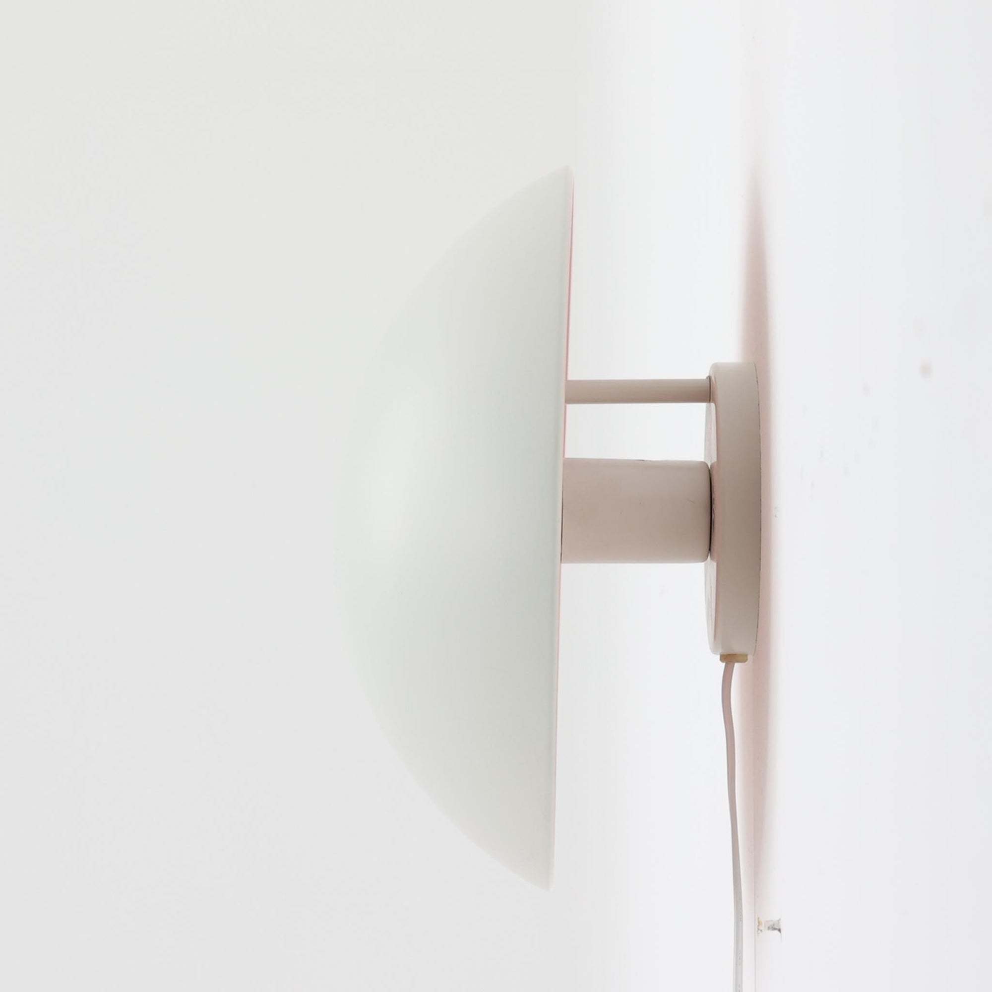 Poul Henningsenがデザインし、Louis Poulsen社から発表されたウォールランプ「PH ハット」直径30cmです。スチール製の半円形シェードは内側を淡いピンク色に仕上げ、点灯時には柔らかで温かみのある光を壁面に広げます。シンプルながら緻密に計算された光の効果はヘニングセンならではの魅力で、寝室や廊下、リビングの補助照明として最適です。1950年代に誕生したモデルは現在でも高く評価されており、ビンテージならではの風合いと希少性を備えています。元々は2サイズ展開で、本品は現行品には存在しない大サイズの希少モデルです。