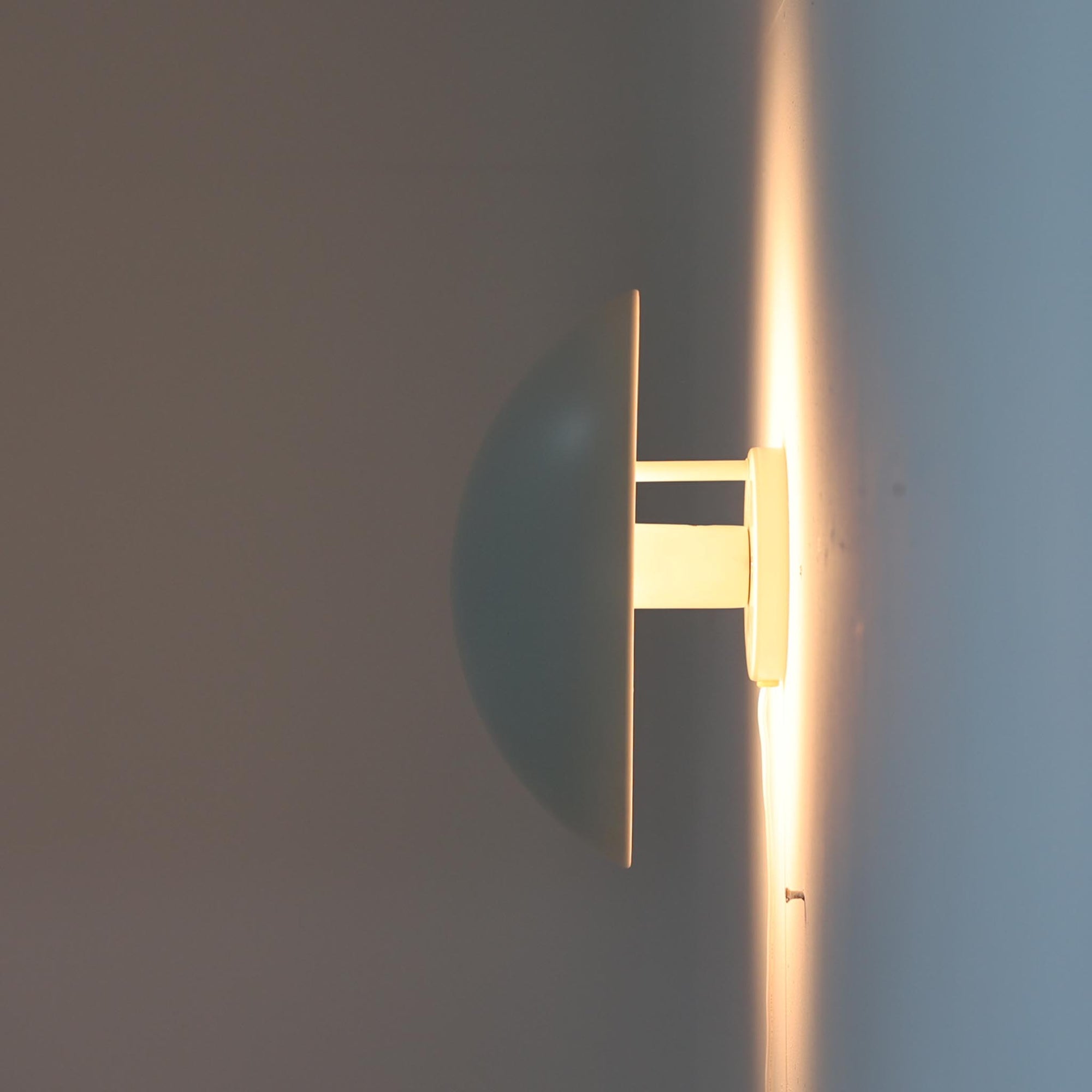 Poul Henningsenがデザインし、Louis Poulsen社から発表されたウォールランプ「PH ハット」直径30cmです。スチール製の半円形シェードは内側を淡いピンク色に仕上げ、点灯時には柔らかで温かみのある光を壁面に広げます。シンプルながら緻密に計算された光の効果はヘニングセンならではの魅力で、寝室や廊下、リビングの補助照明として最適です。1950年代に誕生したモデルは現在でも高く評価されており、ビンテージならではの風合いと希少性を備えています。元々は2サイズ展開で、本品は現行品には存在しない大サイズの希少モデルです。