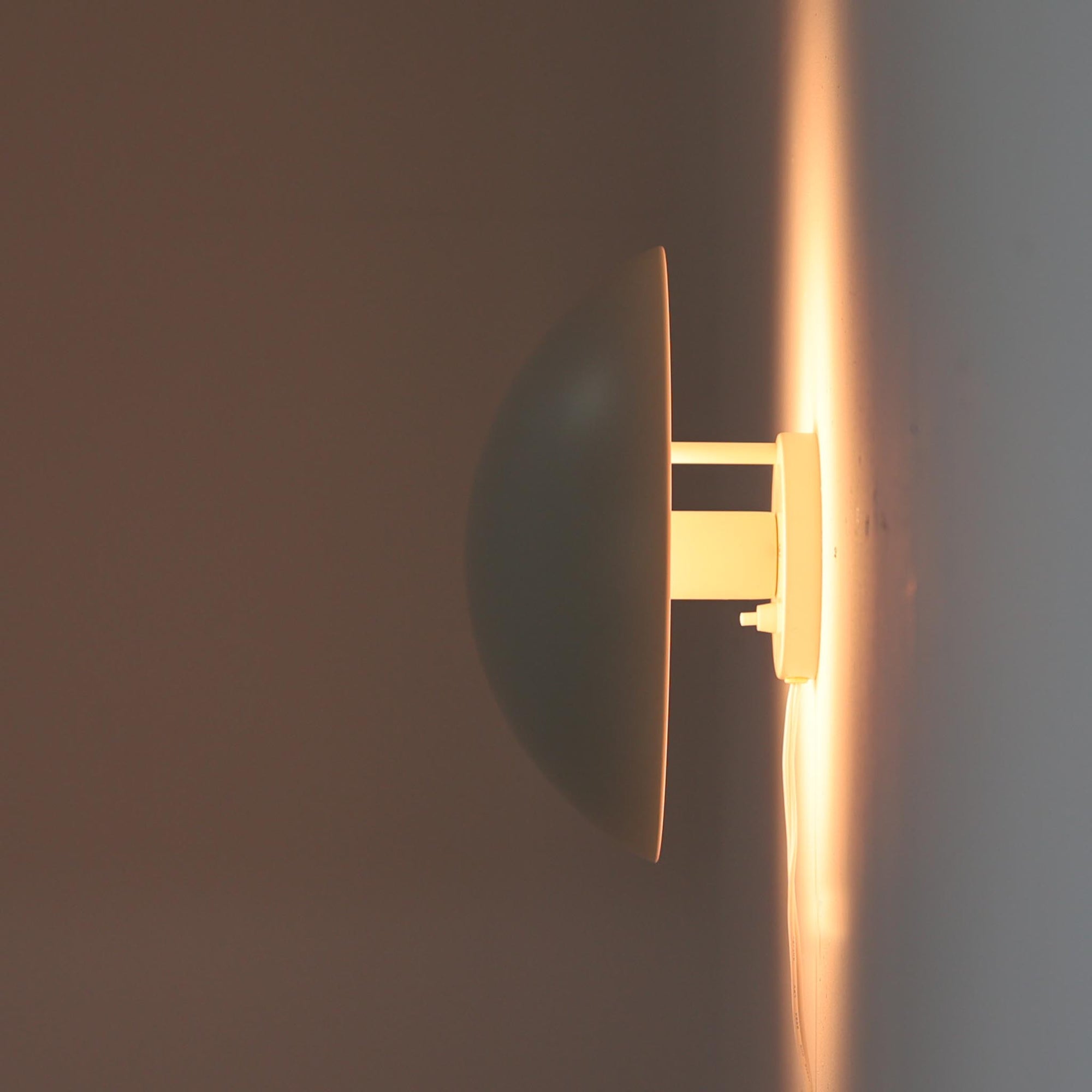 Poul Henningsenがデザインし、Louis Poulsen社から発表されたウォールランプ「PH ハット」直径30cmです。スチール製の半円形シェードは内側を淡いピンク色に仕上げ、点灯時には柔らかで温かみのある光を壁面に広げます。シンプルながら緻密に計算された光の効果はヘニングセンならではの魅力で、寝室や廊下、リビングの補助照明として最適です。1950年代に誕生したモデルは現在でも高く評価されており、ビンテージならではの風合いと希少性を備えています。元々は2サイズ展開で、本品は現行品には存在しない大サイズの希少モデルです。