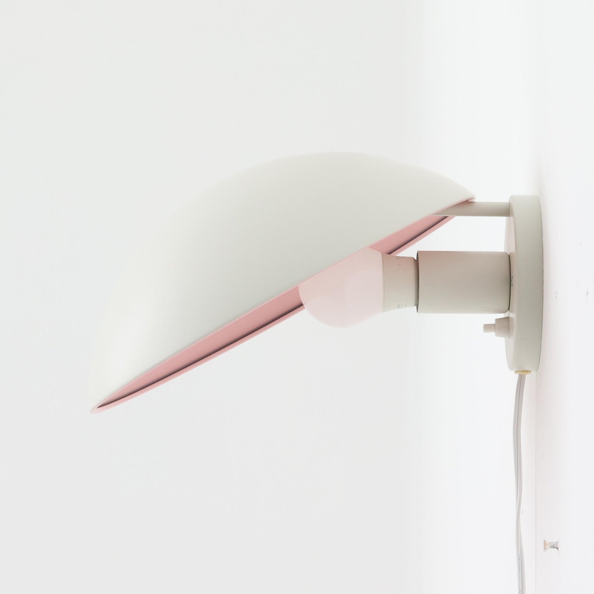 Poul Henningsenがデザインし、Louis Poulsen社から発表されたウォールランプ「PH ハット」直径30cmです。スチール製の半円形シェードは内側を淡いピンク色に仕上げ、点灯時には柔らかで温かみのある光を壁面に広げます。シンプルながら緻密に計算された光の効果はヘニングセンならではの魅力で、寝室や廊下、リビングの補助照明として最適です。1950年代に誕生したモデルは現在でも高く評価されており、ビンテージならではの風合いと希少性を備えています。元々は2サイズ展開で、本品は現行品には存在しない大サイズの希少モデルです。