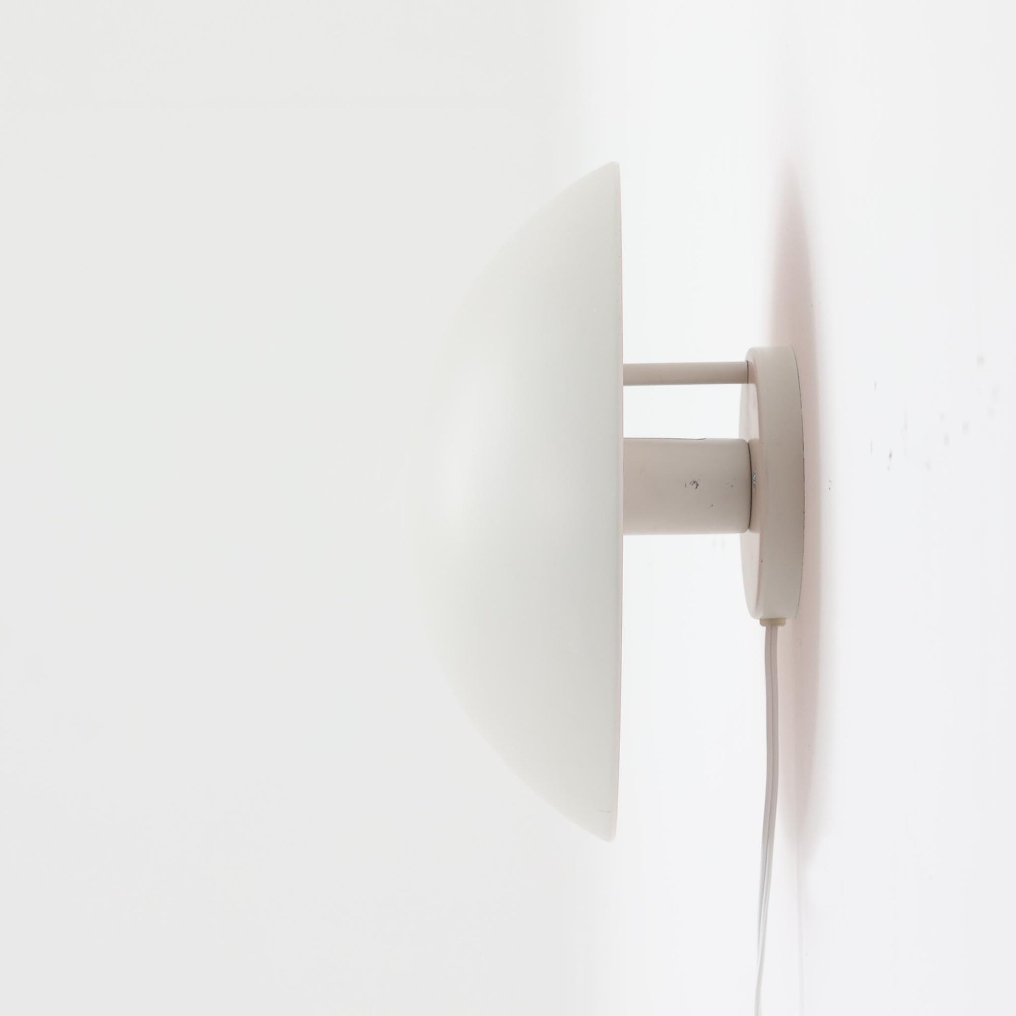 Poul Henningsenがデザインし、Louis Poulsen社から発表されたウォールランプ「PH ハット」直径30cmです。スチール製の半円形シェードは内側を淡いピンク色に仕上げ、点灯時には柔らかで温かみのある光を壁面に広げます。シンプルながら緻密に計算された光の効果はヘニングセンならではの魅力で、寝室や廊下、リビングの補助照明として最適です。1950年代に誕生したモデルは現在でも高く評価されており、ビンテージならではの風合いと希少性を備えています。元々は2サイズ展開で、本品は現行品には存在しない大サイズの希少モデルです。