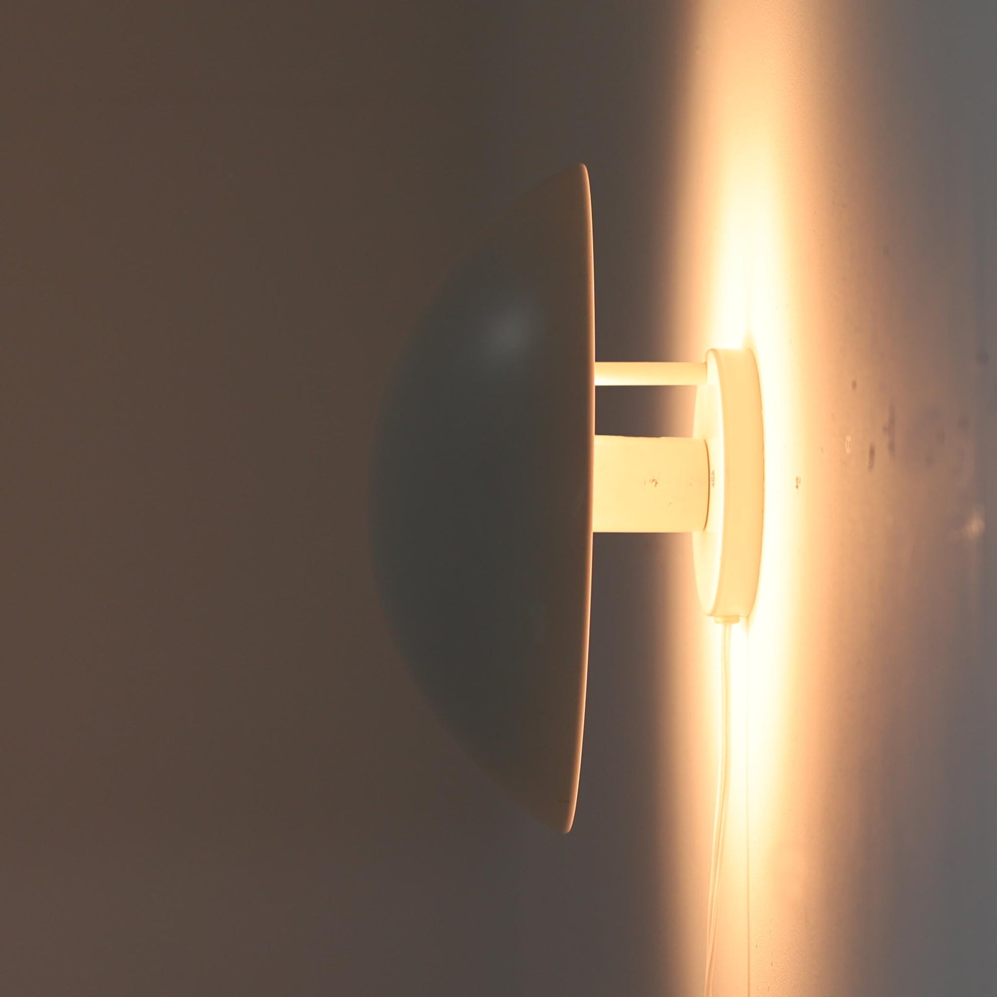 Poul Henningsenがデザインし、Louis Poulsen社から発表されたウォールランプ「PH ハット」直径30cmです。スチール製の半円形シェードは内側を淡いピンク色に仕上げ、点灯時には柔らかで温かみのある光を壁面に広げます。シンプルながら緻密に計算された光の効果はヘニングセンならではの魅力で、寝室や廊下、リビングの補助照明として最適です。1950年代に誕生したモデルは現在でも高く評価されており、ビンテージならではの風合いと希少性を備えています。元々は2サイズ展開で、本品は現行品には存在しない大サイズの希少モデルです。