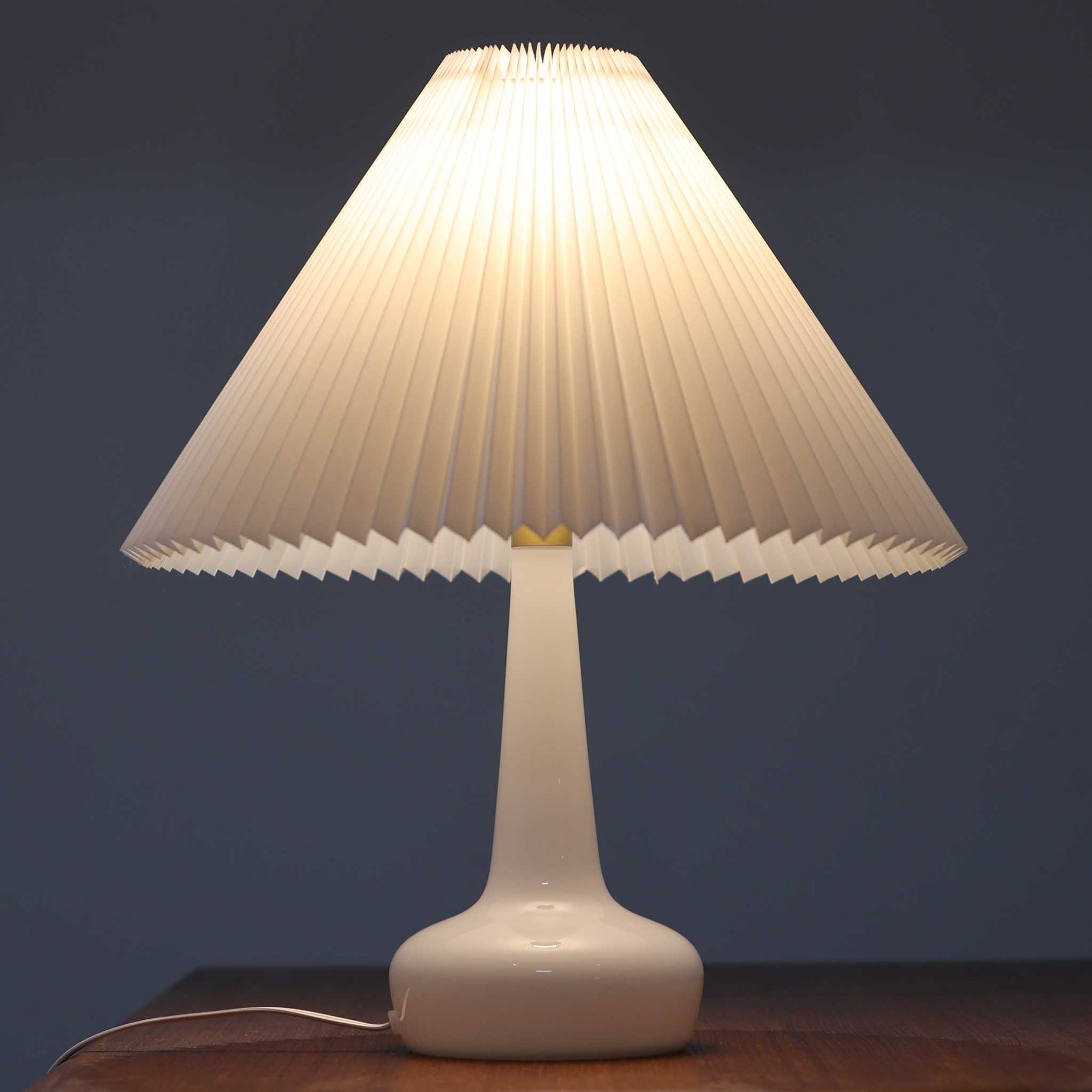 Esben KlintがLe Klintのためにデザインした「Model 311」テーブルランプです。高さ48cmの程よいサイズ感で、ガラスベースと真鍮パーツの組み合わせが美しい一品で、ベース部分はオリジナルです。シェードは後年に交換されたもので、LE KLINT社製のオリジナルではございませんが、同様にプラスチックシートを用いて製作されており、雰囲気を損なうことなく調和しています。点灯時には柔らかな光が広がり、落ち着いた雰囲気を演出。シンプルながらも存在感のあるデザインは、リビングやベッドサイドのアクセントとして最適です。デンマークデザインの伝統と職人技が息づくビンテージ照明です。