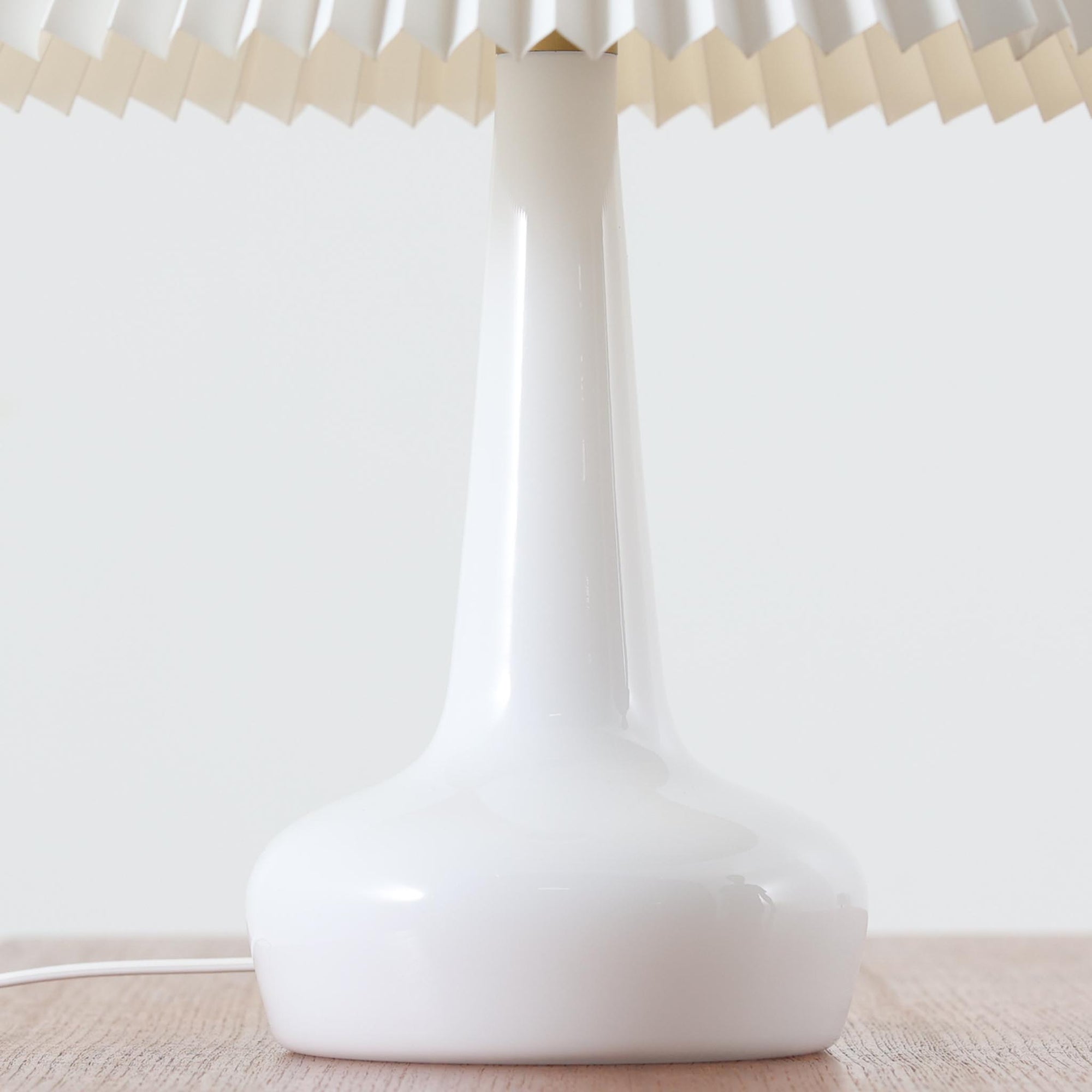 Esben KlintがLe Klintのためにデザインした「Model 311」テーブルランプです。高さ48cmの程よいサイズ感で、ガラスベースと真鍮パーツの組み合わせが美しい一品で、ベース部分はオリジナルです。シェードは後年に交換されたもので、LE KLINT社製のオリジナルではございませんが、同様にプラスチックシートを用いて製作されており、雰囲気を損なうことなく調和しています。点灯時には柔らかな光が広がり、落ち着いた雰囲気を演出。シンプルながらも存在感のあるデザインは、リビングやベッドサイドのアクセントとして最適です。デンマークデザインの伝統と職人技が息づくビンテージ照明です。