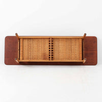 Hans J. WegnerがAndreas Tuckのために手掛けたAT10センターテーブルは、チーク材の天板にオーク材のフレーム、ラタン張りの棚板を組み合わせた、素材使いの美しさが際立つ北欧ビンテージの名作です。直線を基調とした端正なプロポーションの中に、天板縁のやわらかな丸みや、軽やかに抜け感を生むラタン棚が配され、視覚的にも圧迫感のない佇まいに仕上げられています。幅160cmのゆとりあるサイズはリビングの主役として使いやすく、雑誌や小物を収納できる実用性も備え、経年変化により深みを増した木肌が空間に上質な落ち着きをもたらします。なお、天板には反りがあり、大きめのへこみも見られるため、その点を考慮した価格設定としておりますが、ご使用には問題なく、ビンテージならではの風合いとしてご理解いただける方におすすめの一台です。