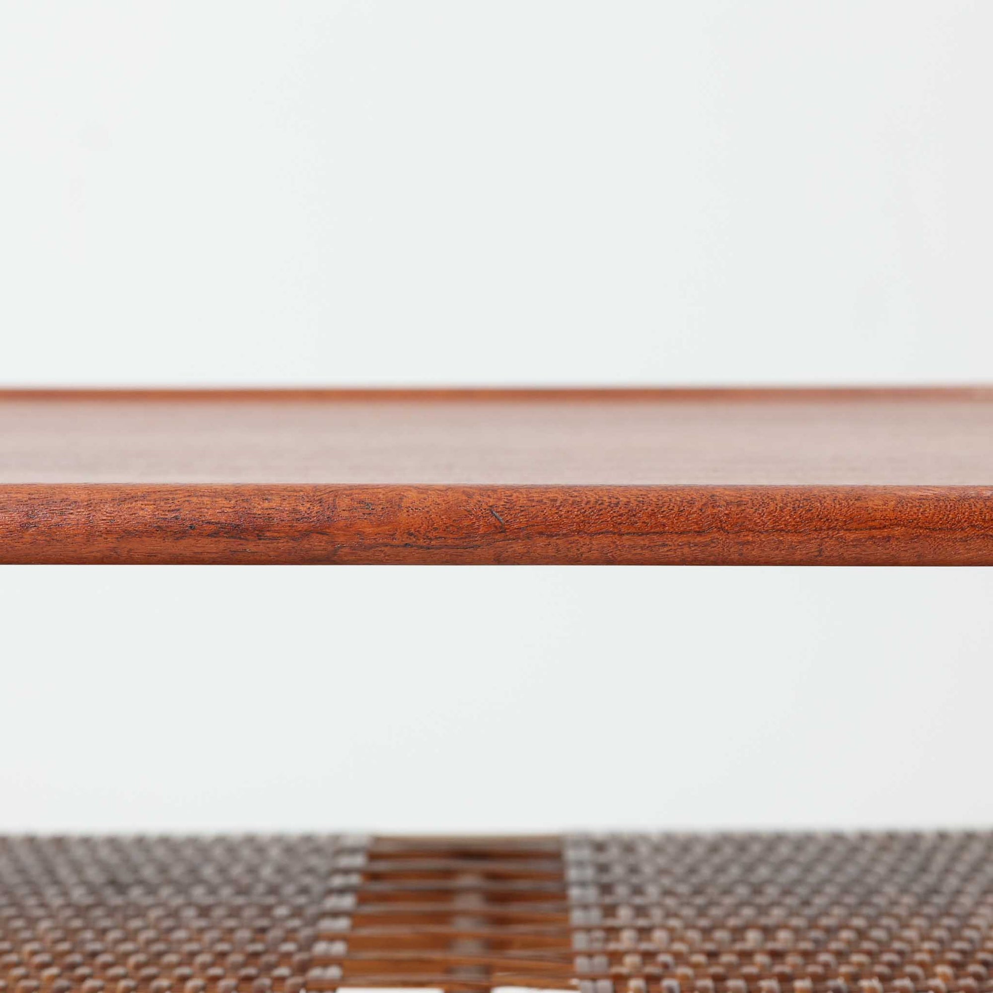 Hans J. WegnerがAndreas Tuckのために手掛けたAT10センターテーブルは、チーク材の天板にオーク材のフレーム、ラタン張りの棚板を組み合わせた、素材使いの美しさが際立つ北欧ビンテージの名作です。直線を基調とした端正なプロポーションの中に、天板縁のやわらかな丸みや、軽やかに抜け感を生むラタン棚が配され、視覚的にも圧迫感のない佇まいに仕上げられています。幅160cmのゆとりあるサイズはリビングの主役として使いやすく、雑誌や小物を収納できる実用性も備え、経年変化により深みを増した木肌が空間に上質な落ち着きをもたらします。なお、天板には反りがあり、大きめのへこみも見られるため、その点を考慮した価格設定としておりますが、ご使用には問題なく、ビンテージならではの風合いとしてご理解いただける方におすすめの一台です。