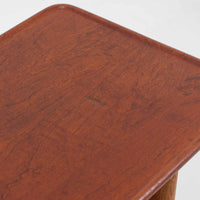 Hans J. WegnerがAndreas Tuckのために手掛けたAT10センターテーブルは、チーク材の天板にオーク材のフレーム、ラタン張りの棚板を組み合わせた、素材使いの美しさが際立つ北欧ビンテージの名作です。直線を基調とした端正なプロポーションの中に、天板縁のやわらかな丸みや、軽やかに抜け感を生むラタン棚が配され、視覚的にも圧迫感のない佇まいに仕上げられています。幅160cmのゆとりあるサイズはリビングの主役として使いやすく、雑誌や小物を収納できる実用性も備え、経年変化により深みを増した木肌が空間に上質な落ち着きをもたらします。なお、天板には反りがあり、大きめのへこみも見られるため、その点を考慮した価格設定としておりますが、ご使用には問題なく、ビンテージならではの風合いとしてご理解いただける方におすすめの一台です。