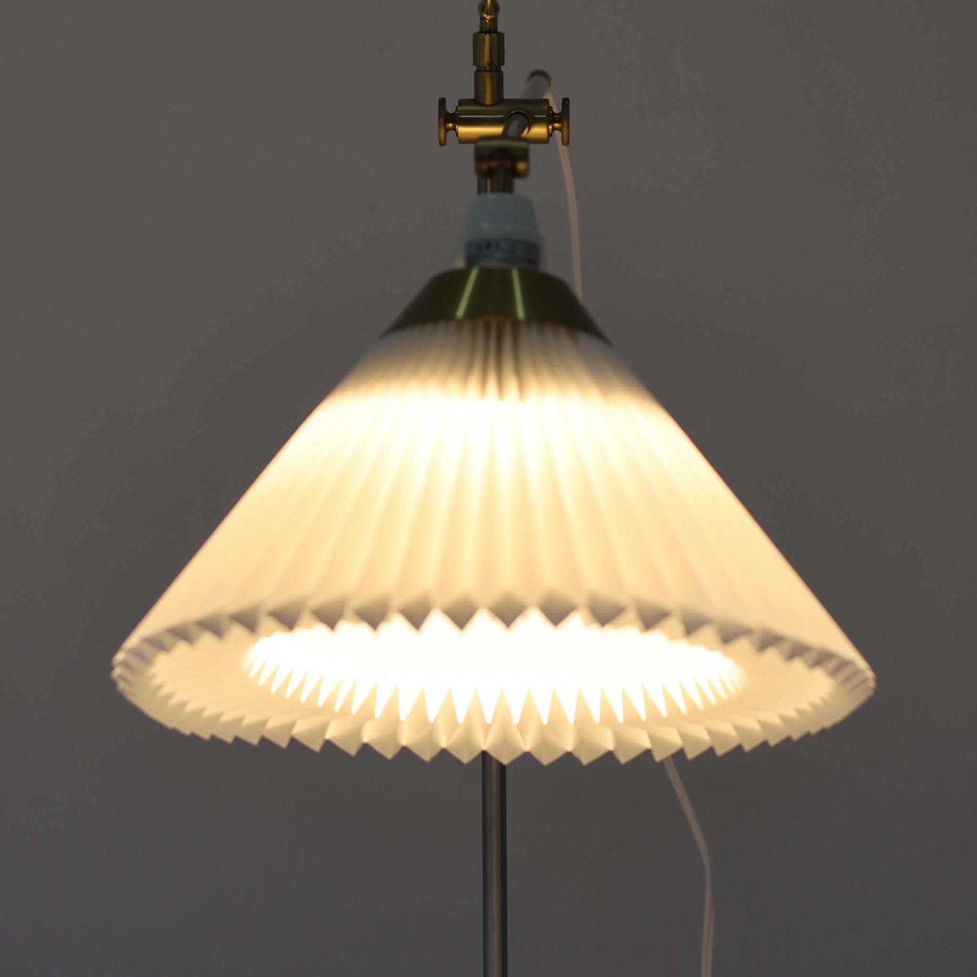 Esben Klintによるデザインで、Le Klint（レ・クリント）より発表されたテーブルランプModel 319です。真鍮とスチールを組み合わせた構造は、堅牢さと洗練された印象を兼ね備え、ハンドメイドのプリーツシェードが柔らかい光を拡散します。高さ75cmの程よいサイズ感とクロスバー構造による可動性が特徴で、デスクやリビングでの読書灯としても実用的です。経年による真鍮の風合いがビンテージらしい魅力を引き立て、空間にクラシカルで上質な雰囲気をもたらします。