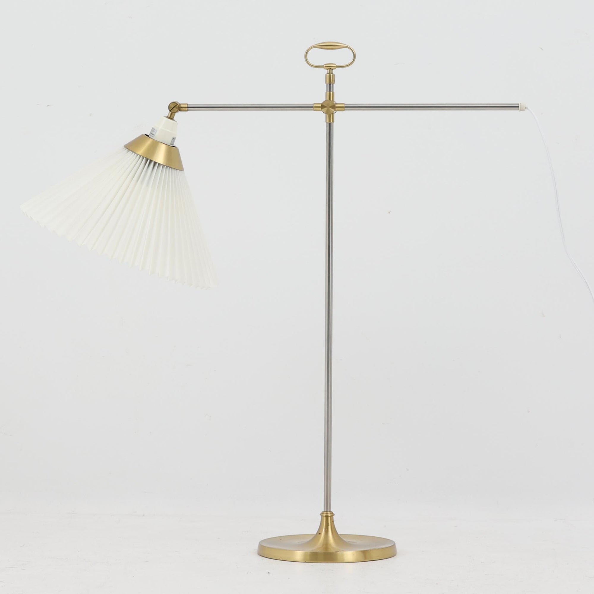 Esben Klintによるデザインで、Le Klint（レ・クリント）より発表されたテーブルランプModel 319です。真鍮とスチールを組み合わせた構造は、堅牢さと洗練された印象を兼ね備え、ハンドメイドのプリーツシェードが柔らかい光を拡散します。高さ75cmの程よいサイズ感とクロスバー構造による可動性が特徴で、デスクやリビングでの読書灯としても実用的です。経年による真鍮の風合いがビンテージらしい魅力を引き立て、空間にクラシカルで上質な雰囲気をもたらします。