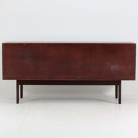 Ole Wanscher（オーレ・ヴァンシャー）がデザインし、P.Jeppesen社より製造された「Rungstedlund」キャビネットです。端正な直線構成と細く伸びた脚部が特徴で、マホガニー材特有の深い色調と気品ある木目が空間に落ち着きをもたらします。内部は棚板とトレイが効率よく配置され、食器から書類収納まで幅広く活用可能。上質な素材使いと精巧な造り込みはヴァンシャー作品ならではで、経年により全体に落ち着いた色調へと変化しており、現地デンマークのオークションで入手した確かな出自を持つ個体です。