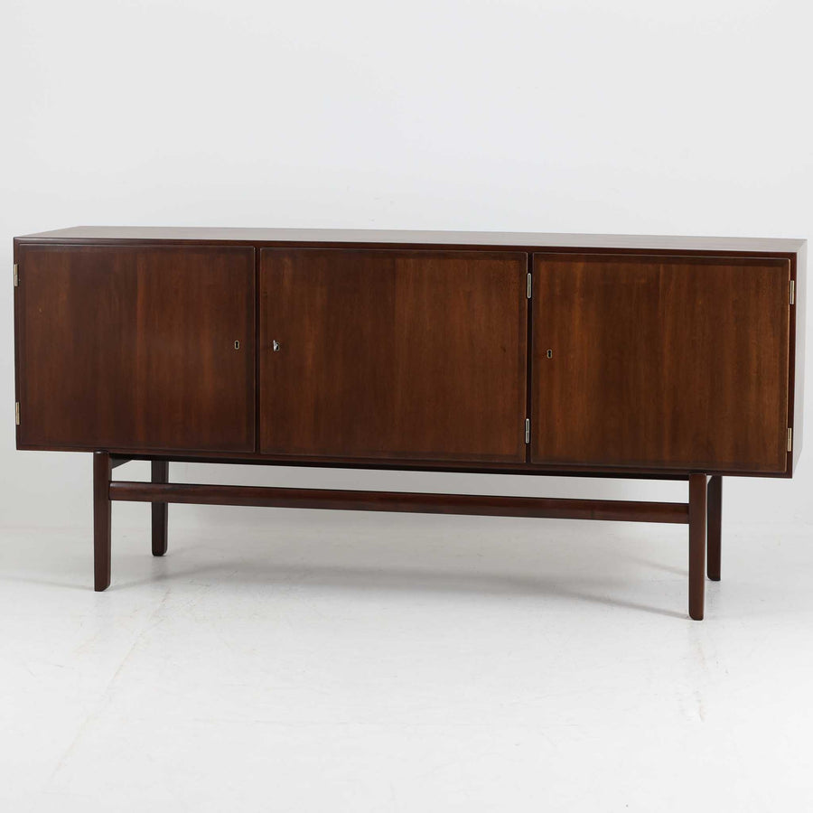 Ole Wanscher（オーレ・ヴァンシャー）がデザインし、P.Jeppesen社より製造された「Rungstedlund」キャビネットです。端正な直線構成と細く伸びた脚部が特徴で、マホガニー材特有の深い色調と気品ある木目が空間に落ち着きをもたらします。内部は棚板とトレイが効率よく配置され、食器から書類収納まで幅広く活用可能。上質な素材使いと精巧な造り込みはヴァンシャー作品ならではで、経年により全体に落ち着いた色調へと変化しており、現地デンマークのオークションで入手した確かな出自を持つ個体です。