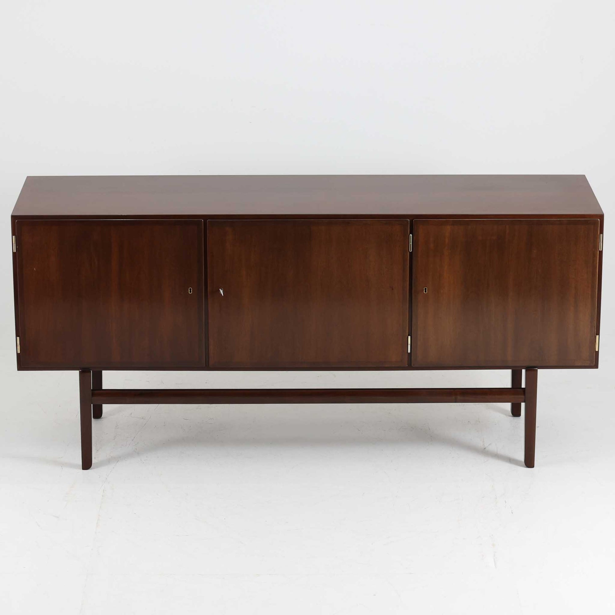 Ole Wanscher（オーレ・ヴァンシャー）がデザインし、P.Jeppesen社より製造された「Rungstedlund」キャビネットです。端正な直線構成と細く伸びた脚部が特徴で、マホガニー材特有の深い色調と気品ある木目が空間に落ち着きをもたらします。内部は棚板とトレイが効率よく配置され、食器から書類収納まで幅広く活用可能。上質な素材使いと精巧な造り込みはヴァンシャー作品ならではで、経年により全体に落ち着いた色調へと変化しており、現地デンマークのオークションで入手した確かな出自を持つ個体です。