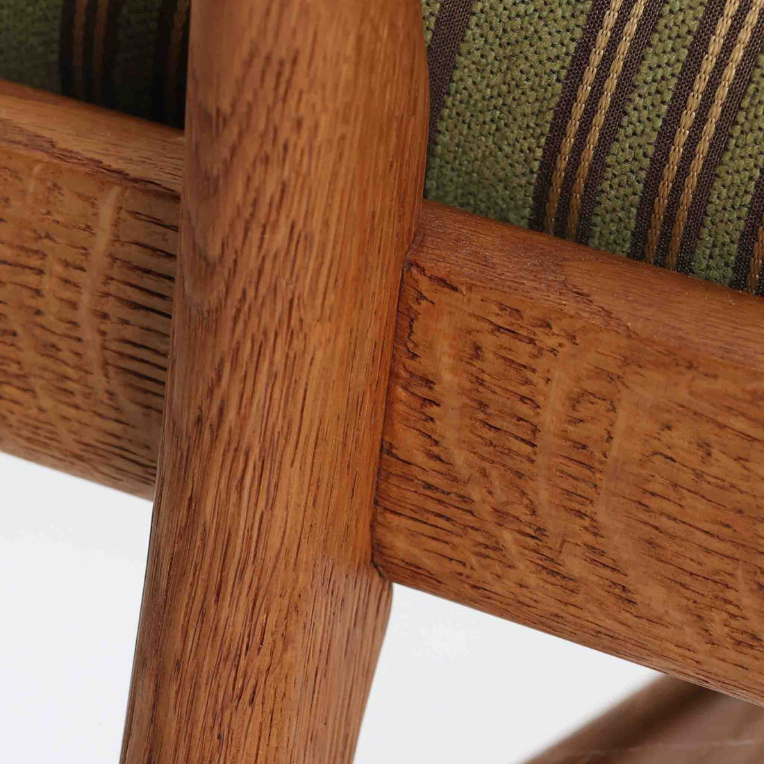 Hans J. Wegner（ハンス・J・ウェグナー）によるイージーチェア「AP16」。デンマークの名門AP stolen社より製造された一脚です。緩やかに傾斜した背もたれと、滑らかに削り出されたアームの曲線が美しく調和し、オーク材の力強い木目と職人技が際立ちます。背面にはブラウン、座面にはグリーンストライプの張地を採用し、上品ながらも温かみのある印象を与えます。現地デンマークのオークションで入手した確かな出自を持つ本品は、読書やくつろぎの時間をより豊かなものにしてくれます。経年による木部の風合いがさらに深みを加えています。