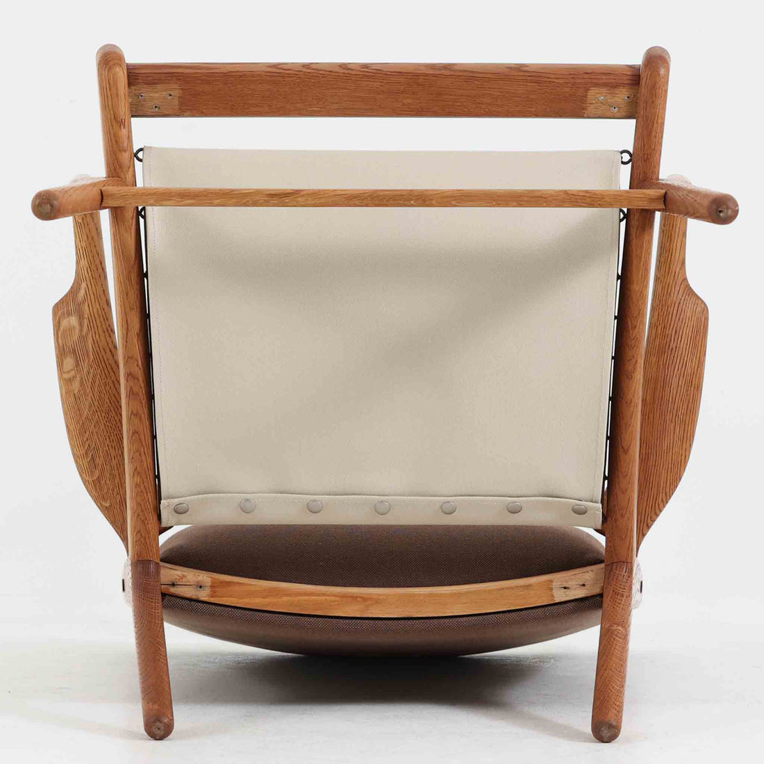 Hans J. Wegner（ハンス・J・ウェグナー）によるイージーチェア「AP16」。デンマークの名門AP stolen社より製造された一脚です。緩やかに傾斜した背もたれと、滑らかに削り出されたアームの曲線が美しく調和し、オーク材の力強い木目と職人技が際立ちます。背面にはブラウン、座面にはグリーンストライプの張地を採用し、上品ながらも温かみのある印象を与えます。現地デンマークのオークションで入手した確かな出自を持つ本品は、読書やくつろぎの時間をより豊かなものにしてくれます。経年による木部の風合いがさらに深みを加えています。