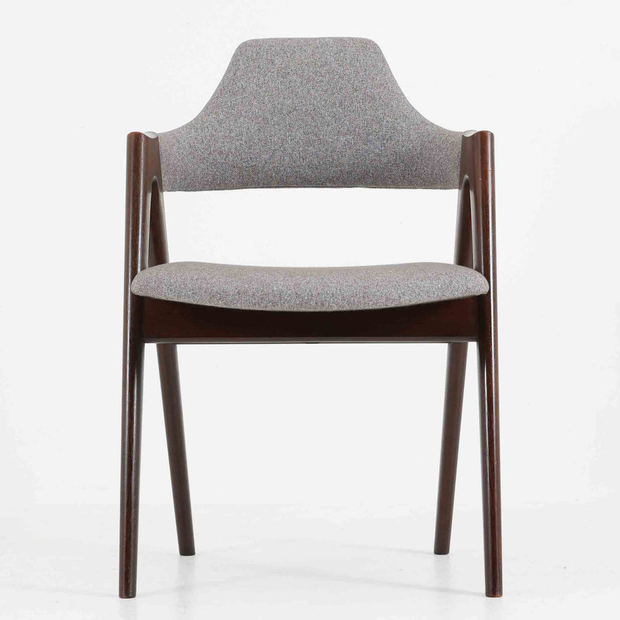 デンマークのデザイナー、Kai Kristiansen（カイ・クリスチャンセン）による「コンパスチェア」。SVA Mobler社より製造された代表作のひとつです。名の通りコンパスの脚を思わせる美しい角度を持つフレーム構造が特徴で、木部にはステイン塗装された濃い色味のオーク材が使用されています。背もたれからアームへと流れるようなラインが柔らかく、身体を包み込むような快適な座り心地を実現。落ち着いたグレーの張地が空間に馴染みます。北欧デザインの美と機能が融合した名作チェアです。