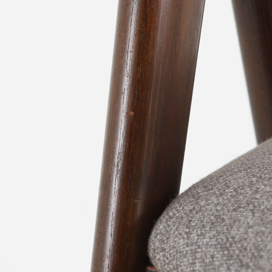 デンマークのデザイナー、Kai Kristiansen（カイ・クリスチャンセン）による「コンパスチェア」。SVA Mobler社より製造された代表作のひとつです。名の通りコンパスの脚を思わせる美しい角度を持つフレーム構造が特徴で、木部にはステイン塗装された濃い色味のオーク材が使用されています。背もたれからアームへと流れるようなラインが柔らかく、身体を包み込むような快適な座り心地を実現。落ち着いたグレーの張地が空間に馴染みます。北欧デザインの美と機能が融合した名作チェアです。