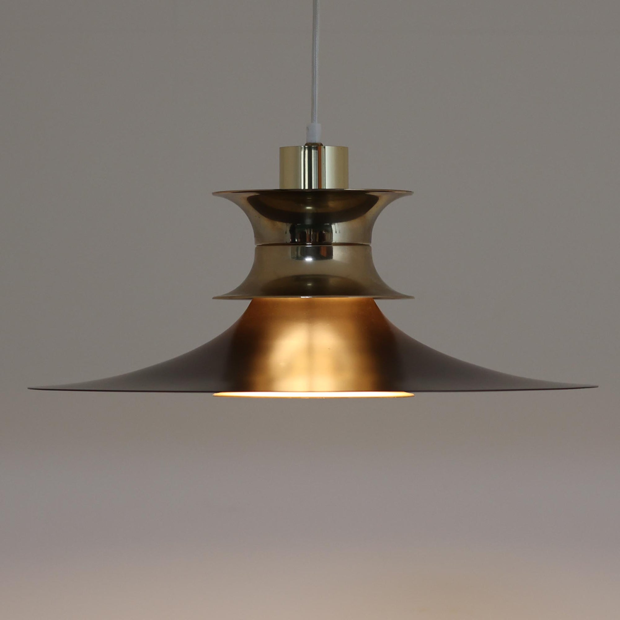 Strini Belysningによる本品は、直径49cmの大きめサイズが特徴のペンダントライトで、アルミ製シェードと真鍮色パーツのコントラストが美しい北欧ビンテージ品です。緩やかに広がるフォルムが光を柔らかく拡散し、ダイニングやリビングなど空間全体を穏やかに照らします。経年により深まった金属の質感がビンテージならではの存在感を放ち、シンプルな構造ながら職人技を感じさせる仕上げが魅力です。大きめのサイズ感を活かして天井から低めに吊るすと、インテリアの主役として空間に上質な雰囲気を添えてくれます。