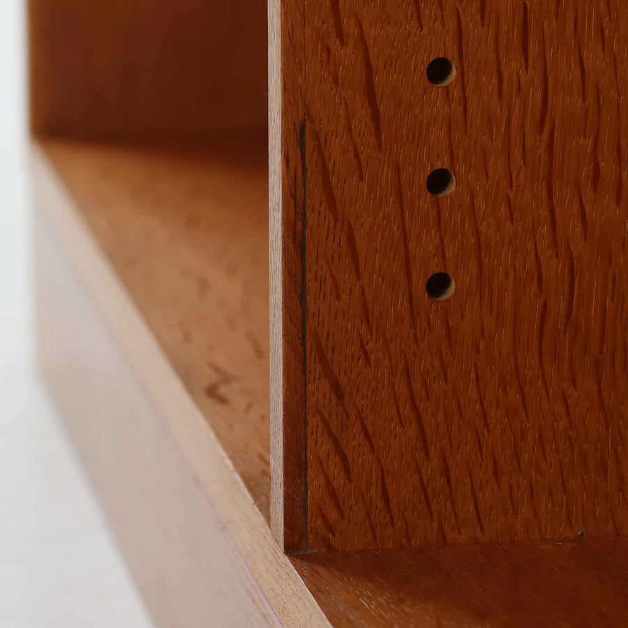 Borge Mogensen（ボーエ・モーエンセン）によるFDB社製のブックシェルフです。良質なオーク材で、温かみのある色合いと堅牢な造りが魅力です。幅122cmのワイドなサイズで、書籍や雑誌の収納はもちろん、オブジェやコレクションのディスプレイにも適しています。シンプルで直線的なフォルムは北欧家具らしい機能美を感じさせ、経年によって増した深い色艶がビンテージならではの存在感を放ちます。書斎やリビングにおいて実用性と美観を兼ね備えた一台です。