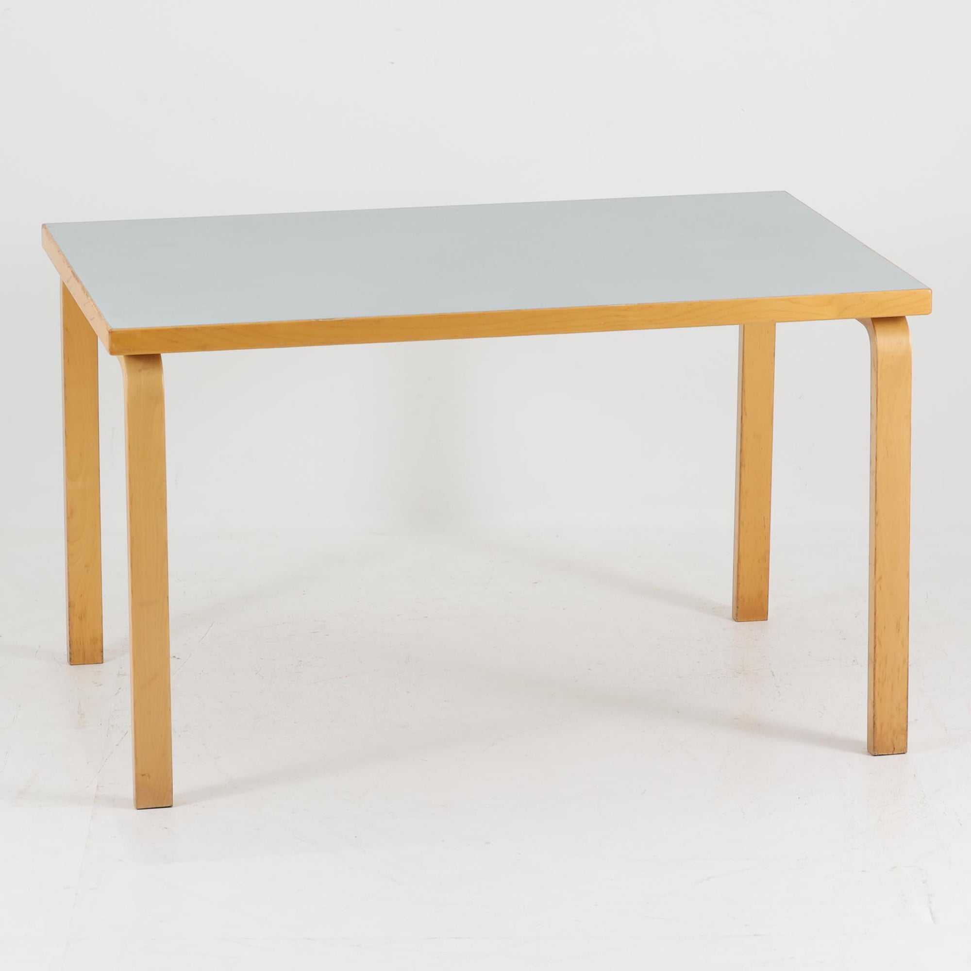 Alvar AaltoがデザインしArtek社より製造されたこちらのダイニングテーブルは、天板に落ち着いたグレートーンのリノリウム、脚部に美しい木肌のバーチ材を用いた北欧モダンデザインの名作で、L字型に曲げられた脚部がアアルトらしい柔らかな造形美を感じさせます。幅120cmの使い勝手のよいサイズ感で、ダイニングやワークスペースにもしっくりと馴染み、天板裏面には脚の付け替え跡が見られ、アアルト製品が多く採用されていたデンマークの公共施設で丁寧に使用されていた個体です。機能美と素材感のバランスに優れた一台です。