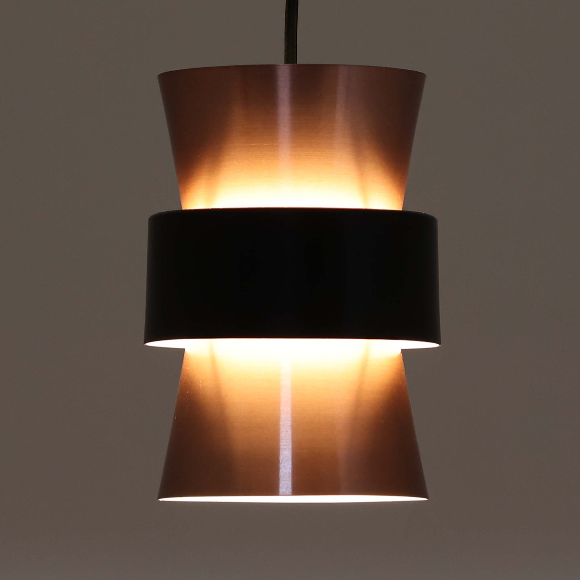 Jo HammerborgがFog & Morup社のためにデザインした直径14cmの小ぶりなペンダントライトです。アルミ製のシェードは上下に広がる砂時計のようなフォルムに、中央のブラックバンドがアクセントとなったモダンなデザイン。点灯時には光が上下にやわらかく広がり、陰影の美しい表情を見せます。コンパクトサイズのためダイニングで複数吊り下げての使用や、玄関・書斎のポイントライトとしても活躍。北欧ビンテージ照明ならではの洗練された存在感を放ちます。