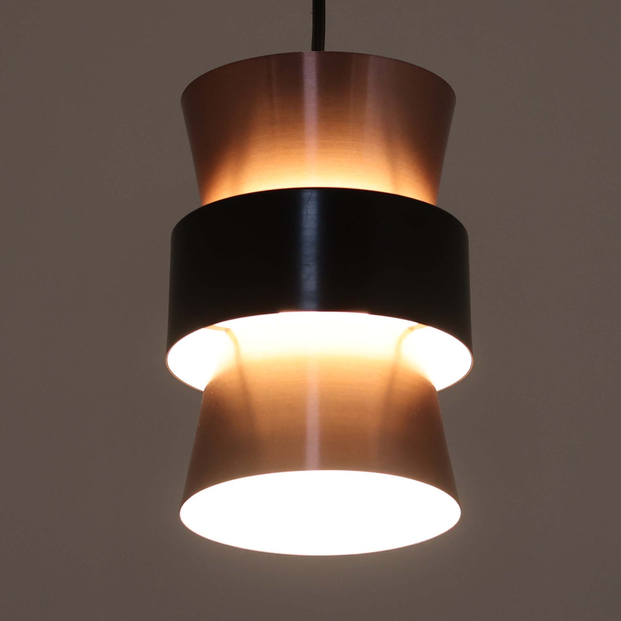 Jo HammerborgがFog &amp; Morup社のためにデザインした直径14cmの小ぶりなペンダントライトです。アルミ製のシェードは上下に広がる砂時計のようなフォルムに、中央のブラックバンドがアクセントとなったモダンなデザイン。点灯時には光が上下にやわらかく広がり、陰影の美しい表情を見せます。コンパクトサイズのためダイニングで複数吊り下げての使用や、玄関・書斎のポイントライトとしても活躍。北欧ビンテージ照明ならではの洗練された存在感を放ちます。