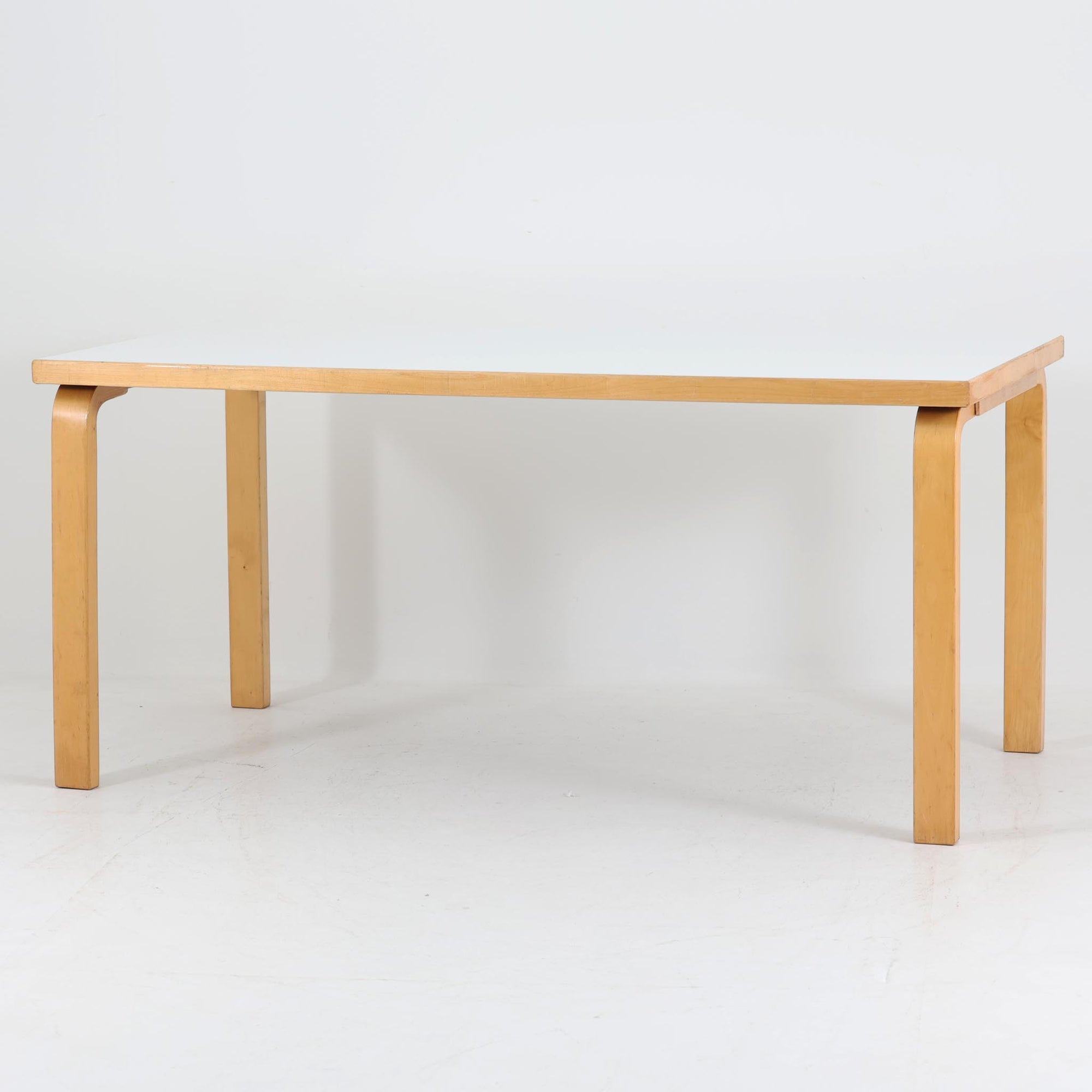 Alvar AaltoがデザインしArtek社より製造されたこちらのダイニングテーブルは、フィンランドモダニズムを象徴する一本。バーチ材の脚部に柔らかくカーブを描くLレッグ構造が取り入れられ、軽やかでありながらも高い強度を実現しています。天板は実用性に優れたホワイトラミネート仕上げで、幅150cmのゆとりあるサイズは家族での食卓やワークスペースにも最適です。幕板の一部に交換がありますが、アアルト製品が多く採用されていたデンマークの公共施設で丁寧に使用されていた個体です。