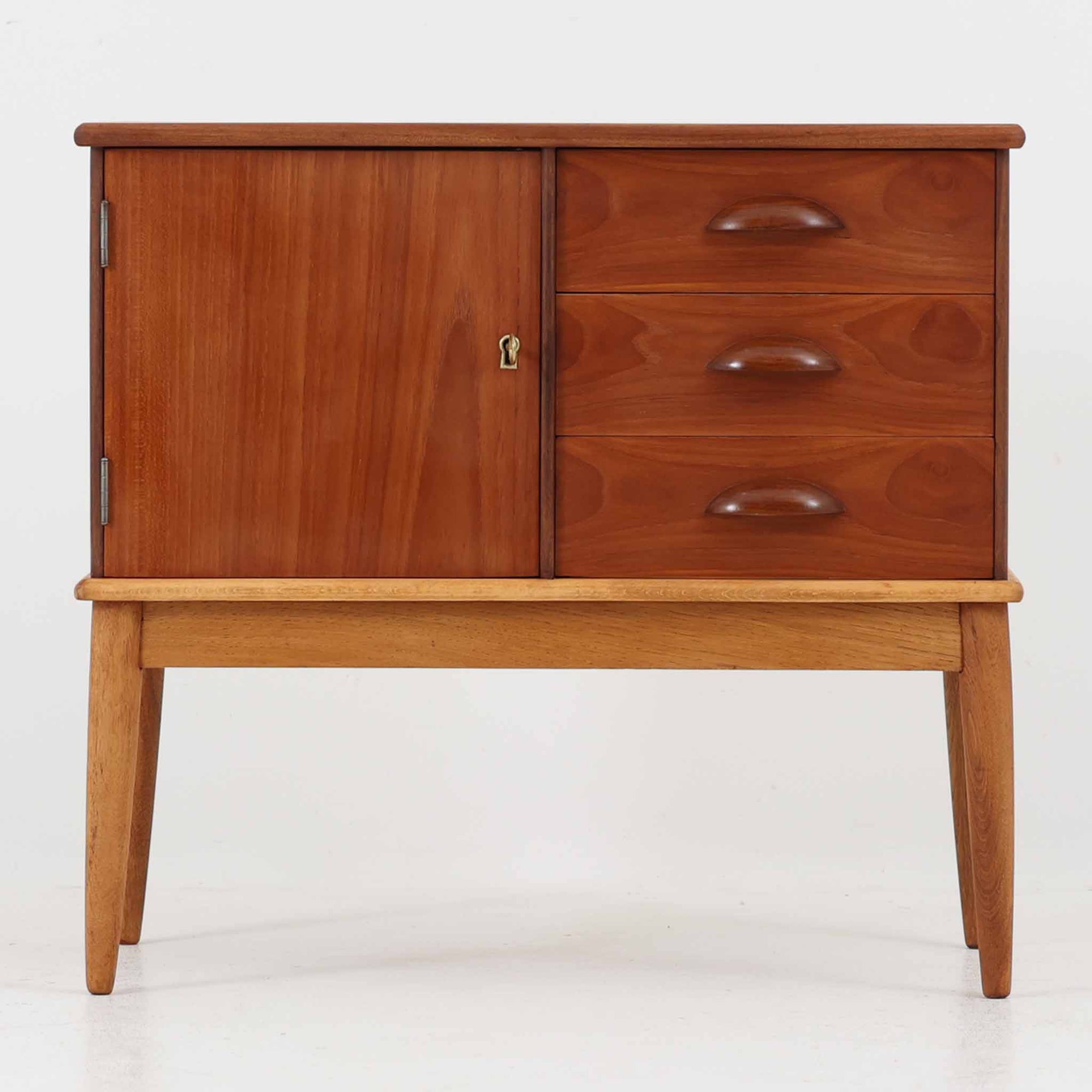 デンマーク製の小ぶりなキャビネットです。チーク材をメインに、オーク材やビーチ材を組み合わせることで、温かみのある色調と軽快な雰囲気を併せ持っています。左側は扉付き収納、右側には3杯の引き出しを備え、実用性とデザイン性を両立。丸みを帯びた取っ手や脚部のテーパーラインが北欧家具らしい柔らかな印象を与えます。幅63cmとコンパクトなサイズで、リビングや寝室、玄関など限られたスペースでも活躍する、ビンテージならではの風合いを持つ一台です。