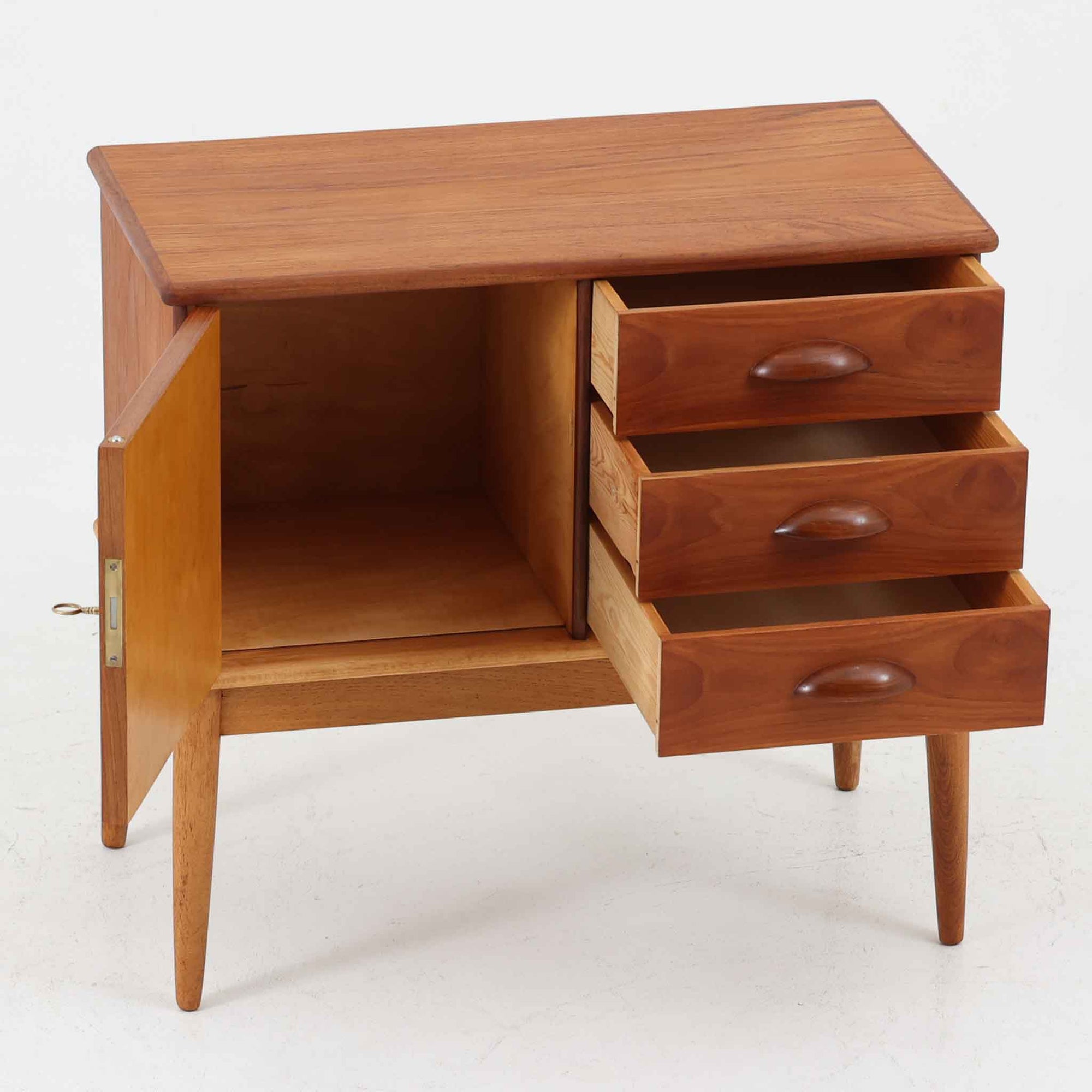 デンマーク製の小ぶりなキャビネットです。チーク材をメインに、オーク材やビーチ材を組み合わせることで、温かみのある色調と軽快な雰囲気を併せ持っています。左側は扉付き収納、右側には3杯の引き出しを備え、実用性とデザイン性を両立。丸みを帯びた取っ手や脚部のテーパーラインが北欧家具らしい柔らかな印象を与えます。幅63cmとコンパクトなサイズで、リビングや寝室、玄関など限られたスペースでも活躍する、ビンテージならではの風合いを持つ一台です。