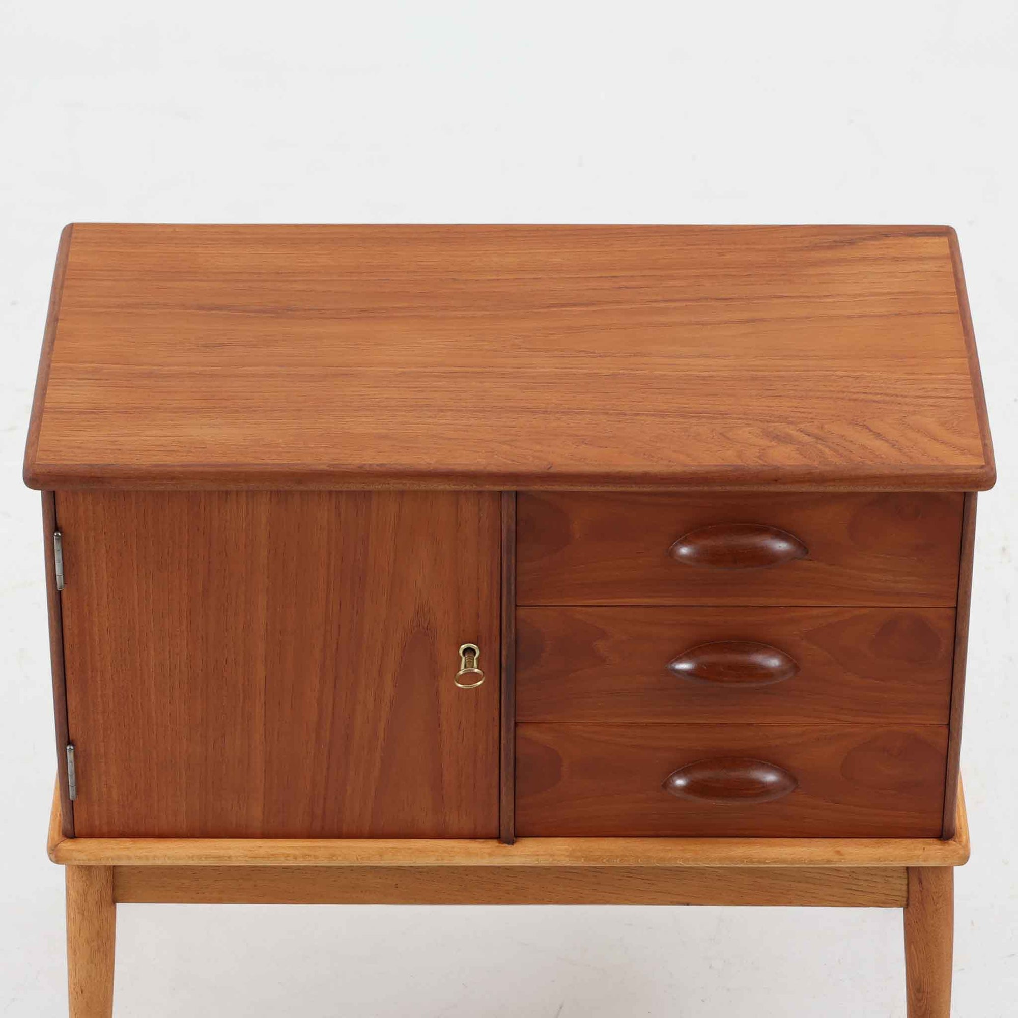 デンマーク製の小ぶりなキャビネットです。チーク材をメインに、オーク材やビーチ材を組み合わせることで、温かみのある色調と軽快な雰囲気を併せ持っています。左側は扉付き収納、右側には3杯の引き出しを備え、実用性とデザイン性を両立。丸みを帯びた取っ手や脚部のテーパーラインが北欧家具らしい柔らかな印象を与えます。幅63cmとコンパクトなサイズで、リビングや寝室、玄関など限られたスペースでも活躍する、ビンテージならではの風合いを持つ一台です。
