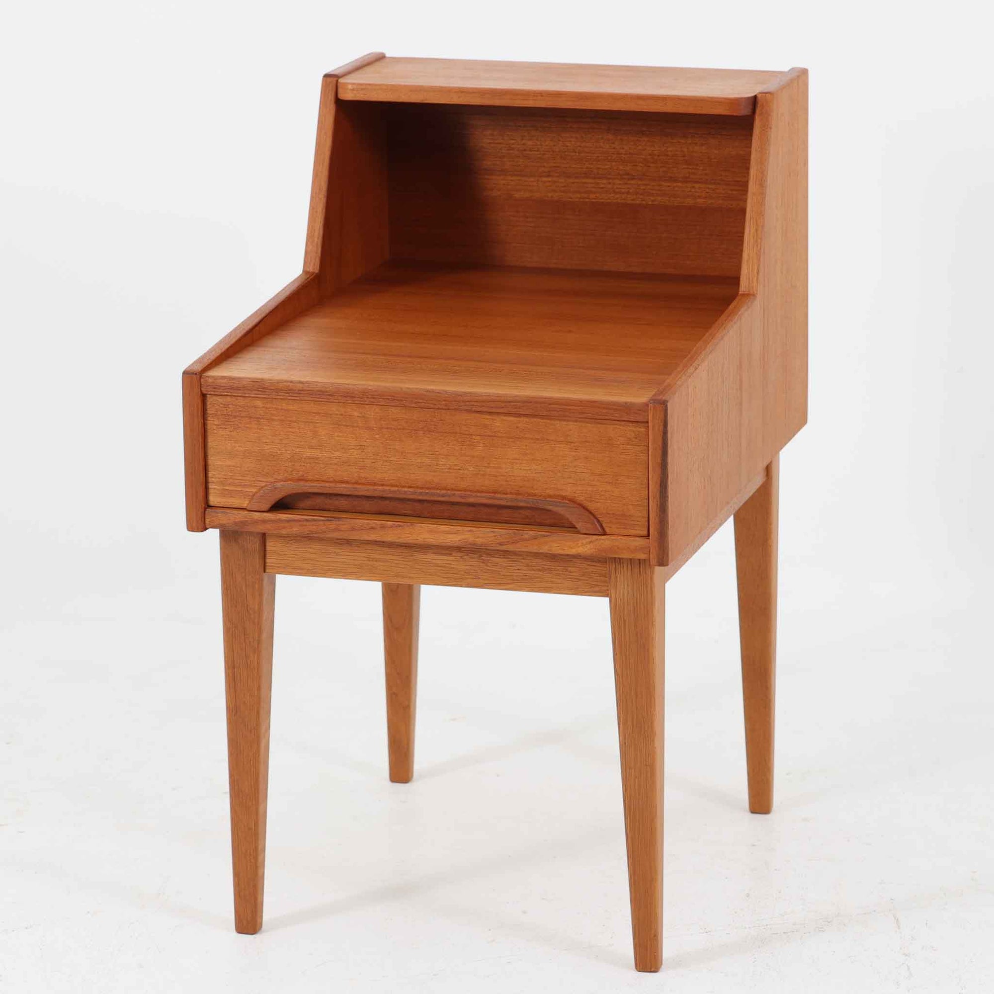 スウェーデン製のこちらのサイドチェストは、チーク材とオーク材を組み合わせた北欧ビンテージ家具で、奥行きのある設計が特徴です。上段は本や小物のディスプレイに、引き出しは日用品の収納に便利で、ナイトテーブルとしての使用にも最適です。直線的で洗練されたフォルムと脚部の無垢材が空間に温もりを添え、年月を経た木肌の風合いが一層の魅力を引き立てます。背面には当時の製造印も残る一点物です。