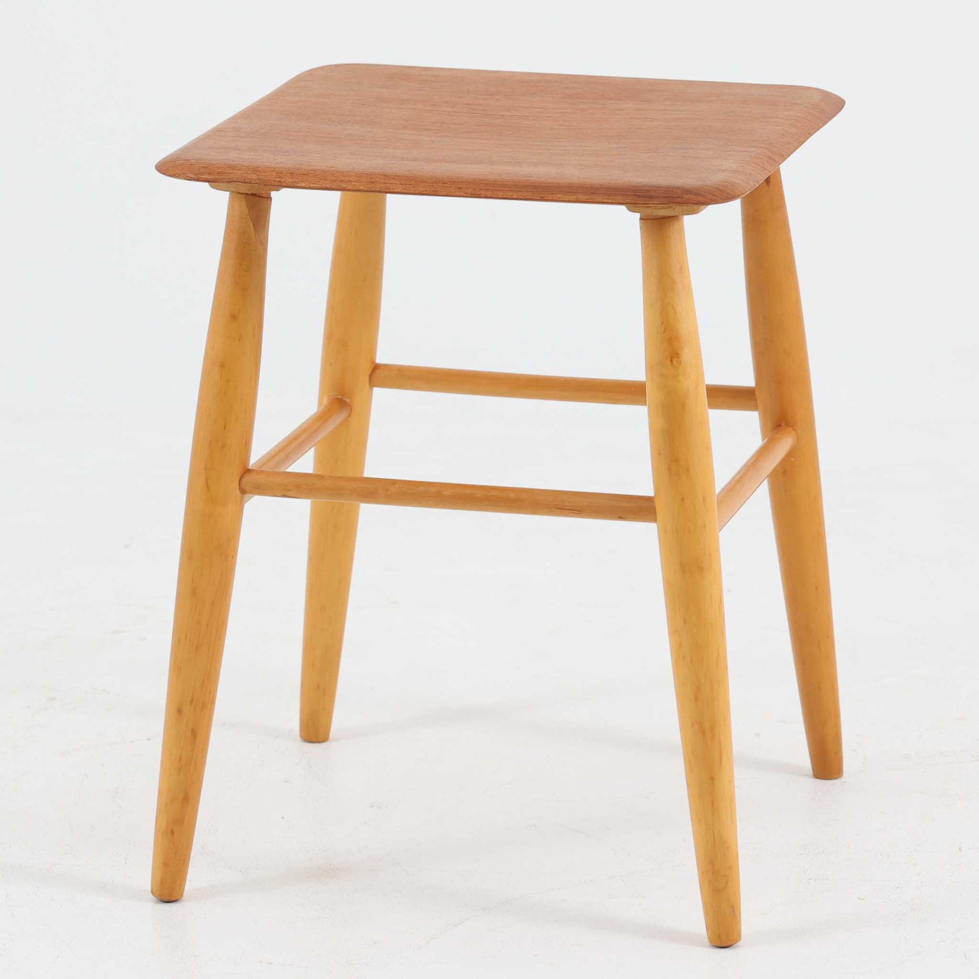 Ilmari Tapiovaaraによってデザインされ、スウェーデンのEDSBY VERKEN社で製造されたFanett（ファネット）スツールは、座面に温かみのあるチーク材、脚部に軽やかなビーチ材を用いた北欧ビンテージらしい一脚です。四方から斜めに伸びる丸脚と貫で構成された堅牢な構造により安定感があり、サイドチェアや花台、小物置きとしても活躍します。使い込むほどに木肌の風合いが増し、空間に上質な趣を添えてくれます。