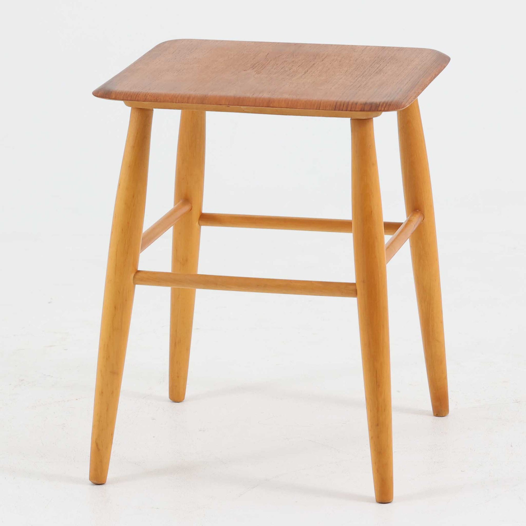 Ilmari Tapiovaaraによってデザインされ、スウェーデンのEDSBY VERKEN社で製造されたFanett（ファネット）スツールは、座面に温かみのあるチーク材、脚部に軽やかなビーチ材を用いた北欧ビンテージらしい一脚です。四方から斜めに伸びる丸脚と貫で構成された堅牢な構造により安定感があり、サイドチェアや花台、小物置きとしても活躍します。使い込むほどに木肌の風合いが増し、空間に上質な趣を添えてくれます。