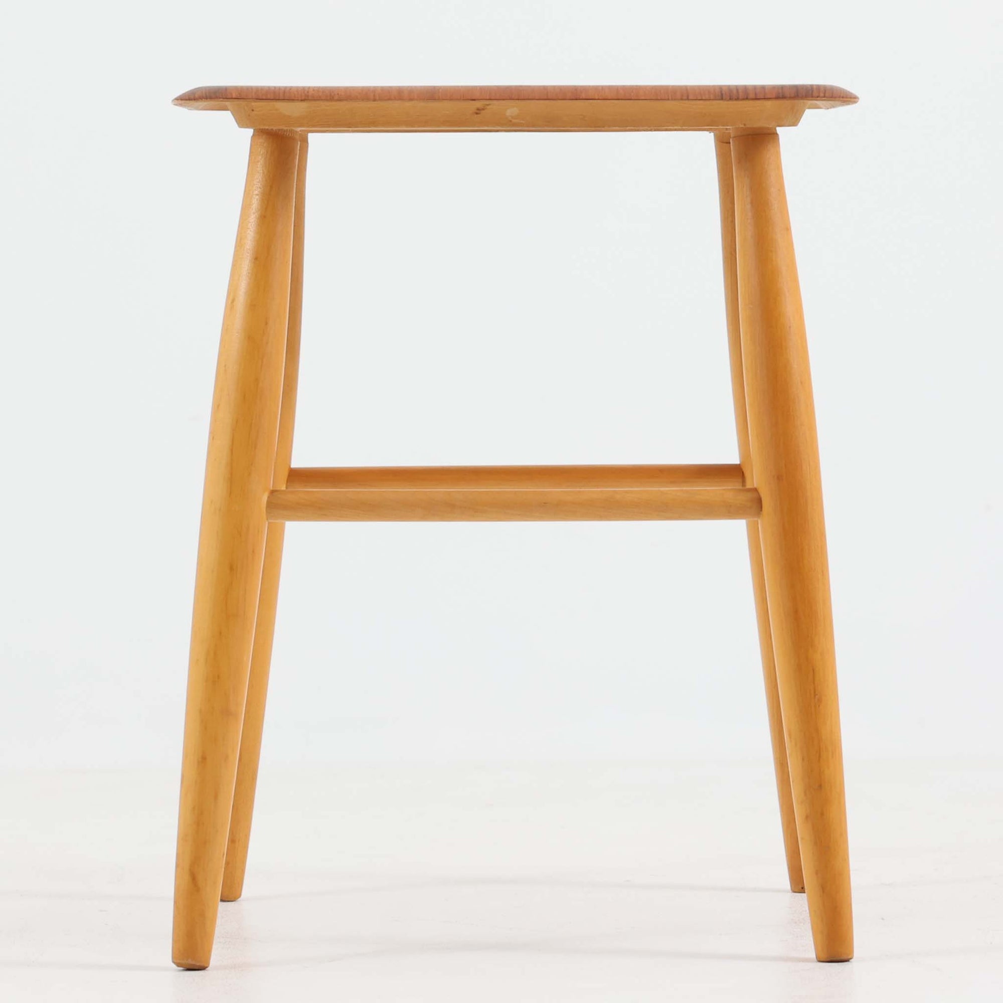 Ilmari Tapiovaaraによってデザインされ、スウェーデンのEDSBY VERKEN社で製造されたFanett（ファネット）スツールは、座面に温かみのあるチーク材、脚部に軽やかなビーチ材を用いた北欧ビンテージらしい一脚です。四方から斜めに伸びる丸脚と貫で構成された堅牢な構造により安定感があり、サイドチェアや花台、小物置きとしても活躍します。使い込むほどに木肌の風合いが増し、空間に上質な趣を添えてくれます。