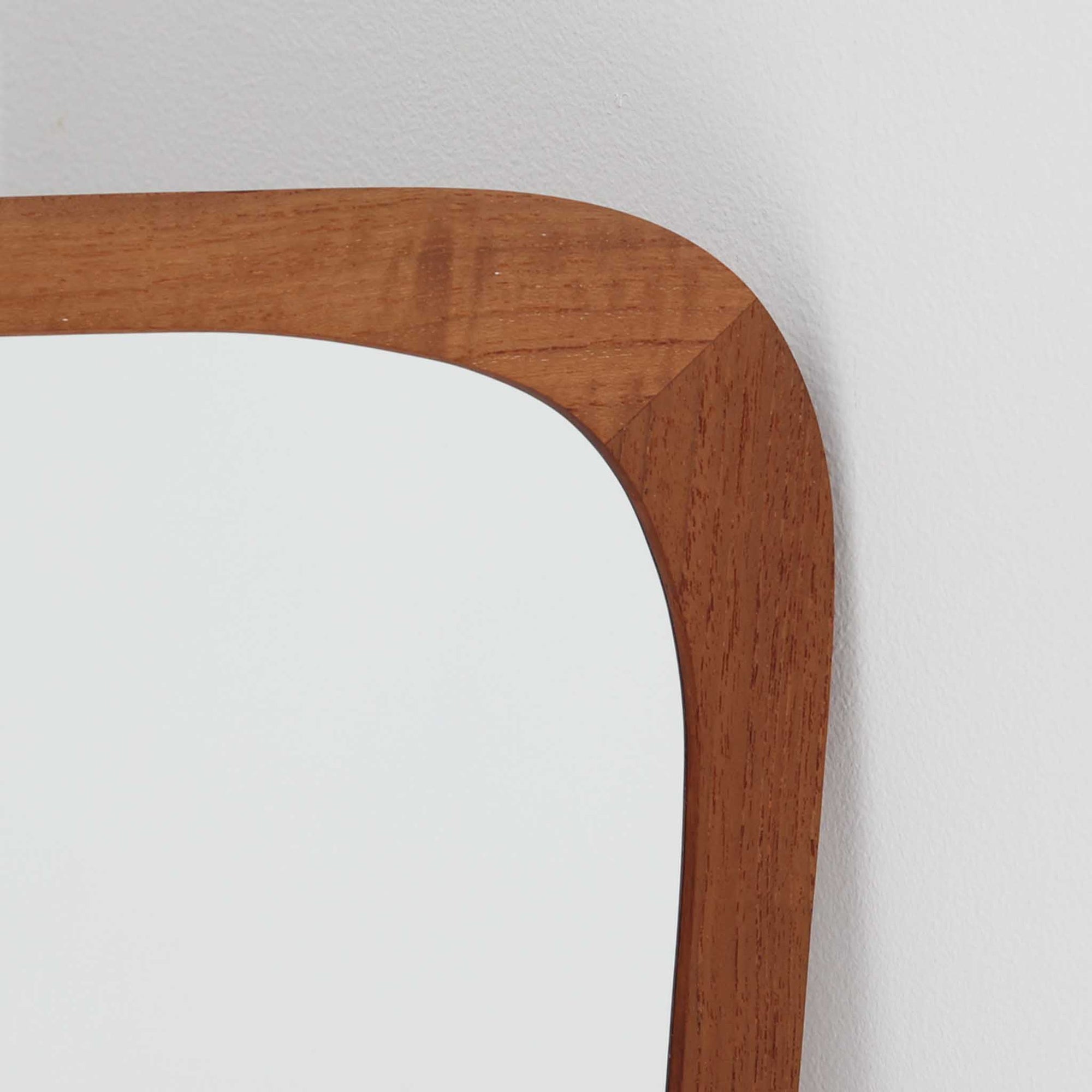 デンマークのAarhus Glasimport og Glassliberi社製による、チーク材フレームの壁掛け／立掛けミラーです。上部がわずかに広がる特徴的な台形フォルムが印象的で、やわらかな曲線を描くフレームが北欧デザインらしい優美さを感じさせます。チーク材のあたたかみのある色合いと美しい木目が空間に自然と溶け込み、玄関や寝室、リビングなどさまざまなシーンで活躍します。経年により深みを増した風合いが、北欧ビンテージらしい落ち着いた存在感を放つ一品です。