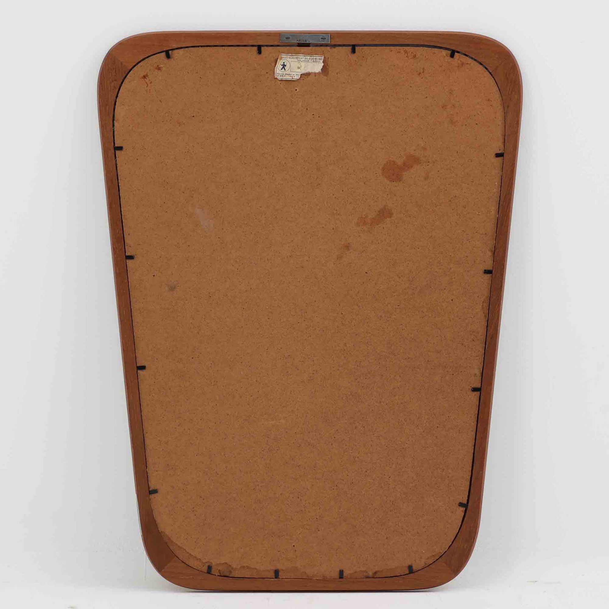 デンマークのAarhus Glasimport og Glassliberi社製による、チーク材フレームの壁掛け／立掛けミラーです。上部がわずかに広がる特徴的な台形フォルムが印象的で、やわらかな曲線を描くフレームが北欧デザインらしい優美さを感じさせます。チーク材のあたたかみのある色合いと美しい木目が空間に自然と溶け込み、玄関や寝室、リビングなどさまざまなシーンで活躍します。経年により深みを増した風合いが、北欧ビンテージらしい落ち着いた存在感を放つ一品です。