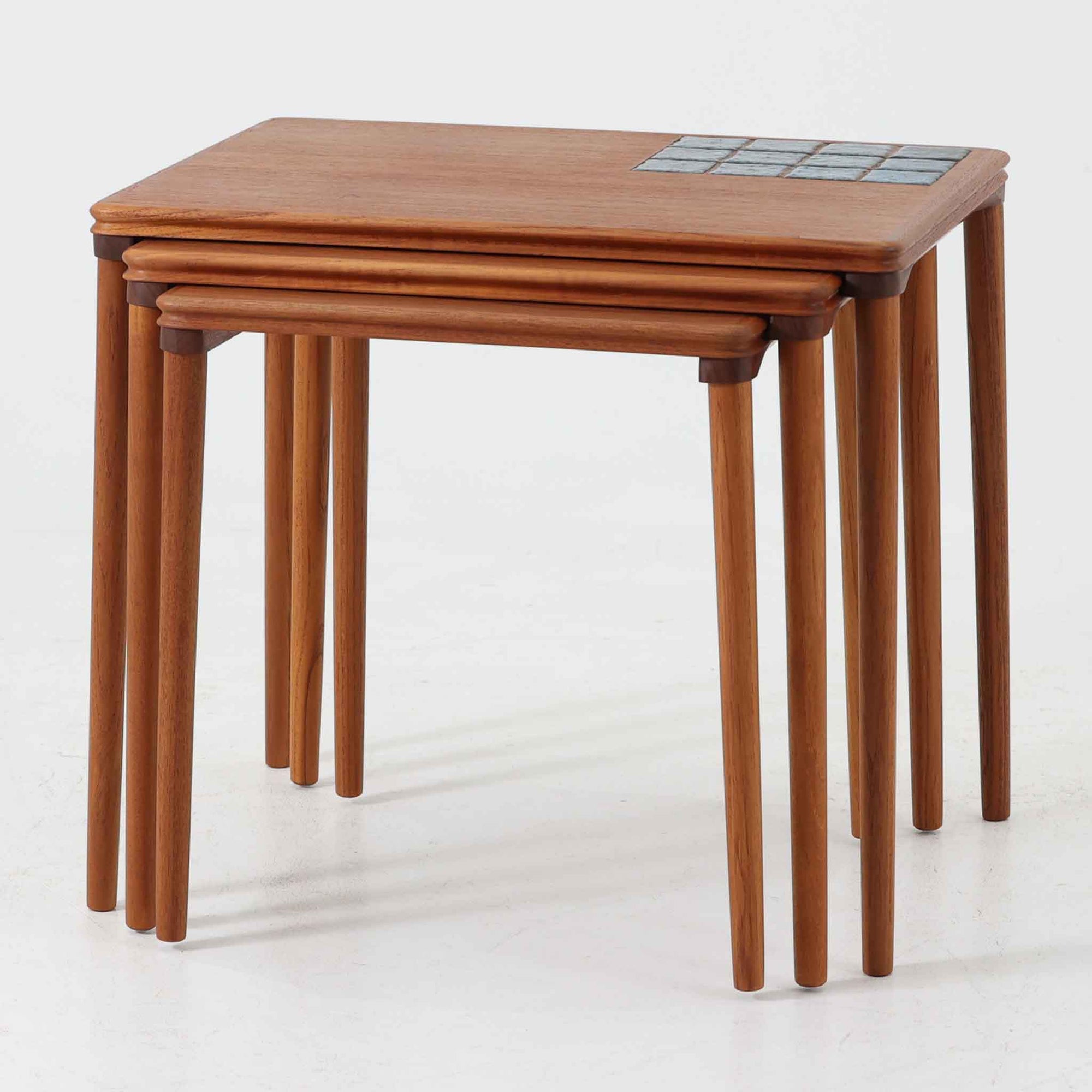 チーク材の温かみある木肌に、落ち着いたブルー系陶磁器タイルをあしらったネストテーブルは、北欧ビンテージらしい実用性と装飾性を兼ね備えたセットです。大小3台を重ねて収納できる合理的な構造で、必要に応じてサイドテーブルや補助台として柔軟に使い分けが可能。角を丸く仕上げた天板や細身の脚部には丁寧な木工技術が感じられ、経年により深みを増した表情が空間に静かな存在感を添えます。