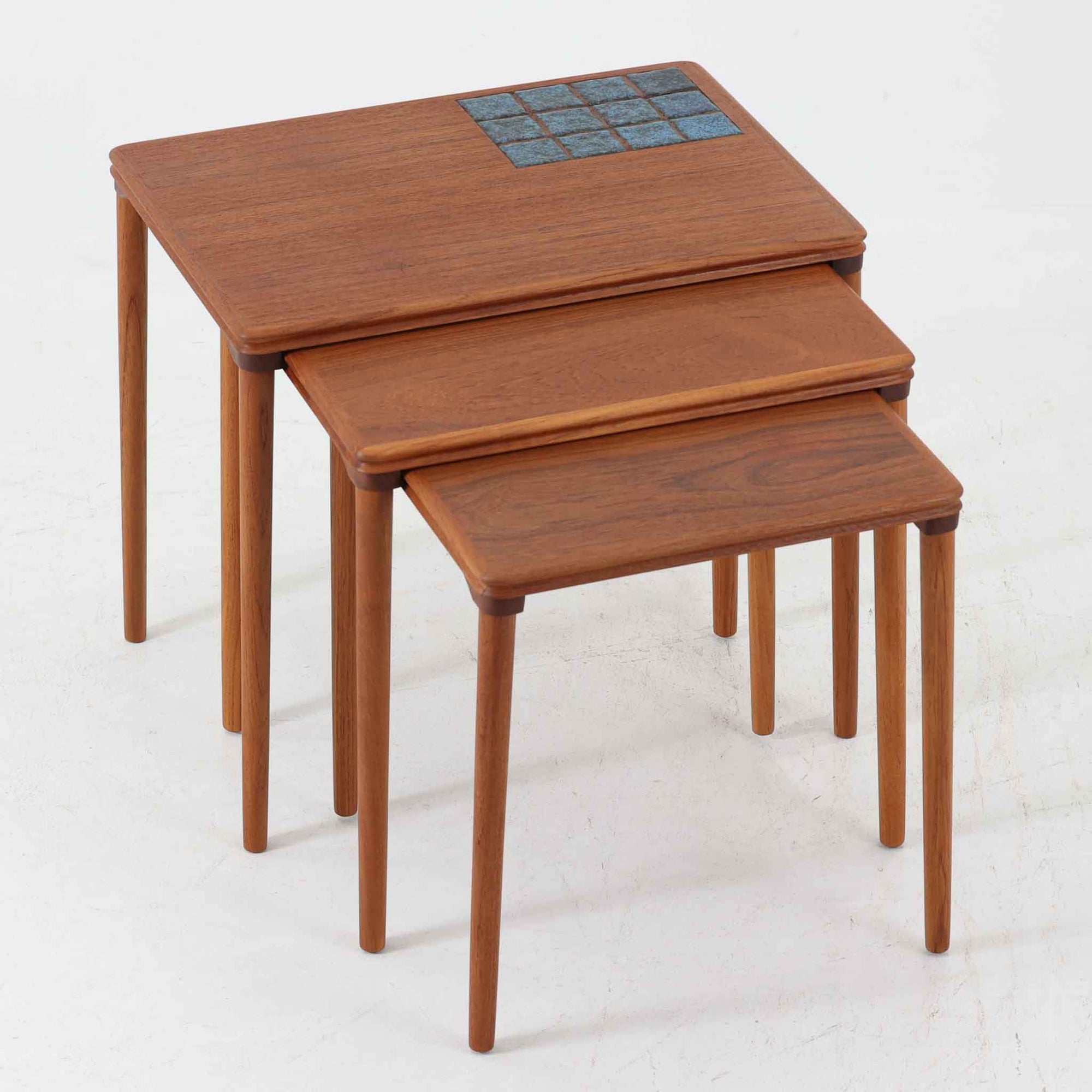 チーク材の温かみある木肌に、落ち着いたブルー系陶磁器タイルをあしらったネストテーブルは、北欧ビンテージらしい実用性と装飾性を兼ね備えたセットです。大小3台を重ねて収納できる合理的な構造で、必要に応じてサイドテーブルや補助台として柔軟に使い分けが可能。角を丸く仕上げた天板や細身の脚部には丁寧な木工技術が感じられ、経年により深みを増した表情が空間に静かな存在感を添えます。