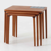 チーク材の温かみある木肌に、落ち着いたブルー系陶磁器タイルをあしらったネストテーブルは、北欧ビンテージらしい実用性と装飾性を兼ね備えたセットです。大小3台を重ねて収納できる合理的な構造で、必要に応じてサイドテーブルや補助台として柔軟に使い分けが可能。角を丸く仕上げた天板や細身の脚部には丁寧な木工技術が感じられ、経年により深みを増した表情が空間に静かな存在感を添えます。