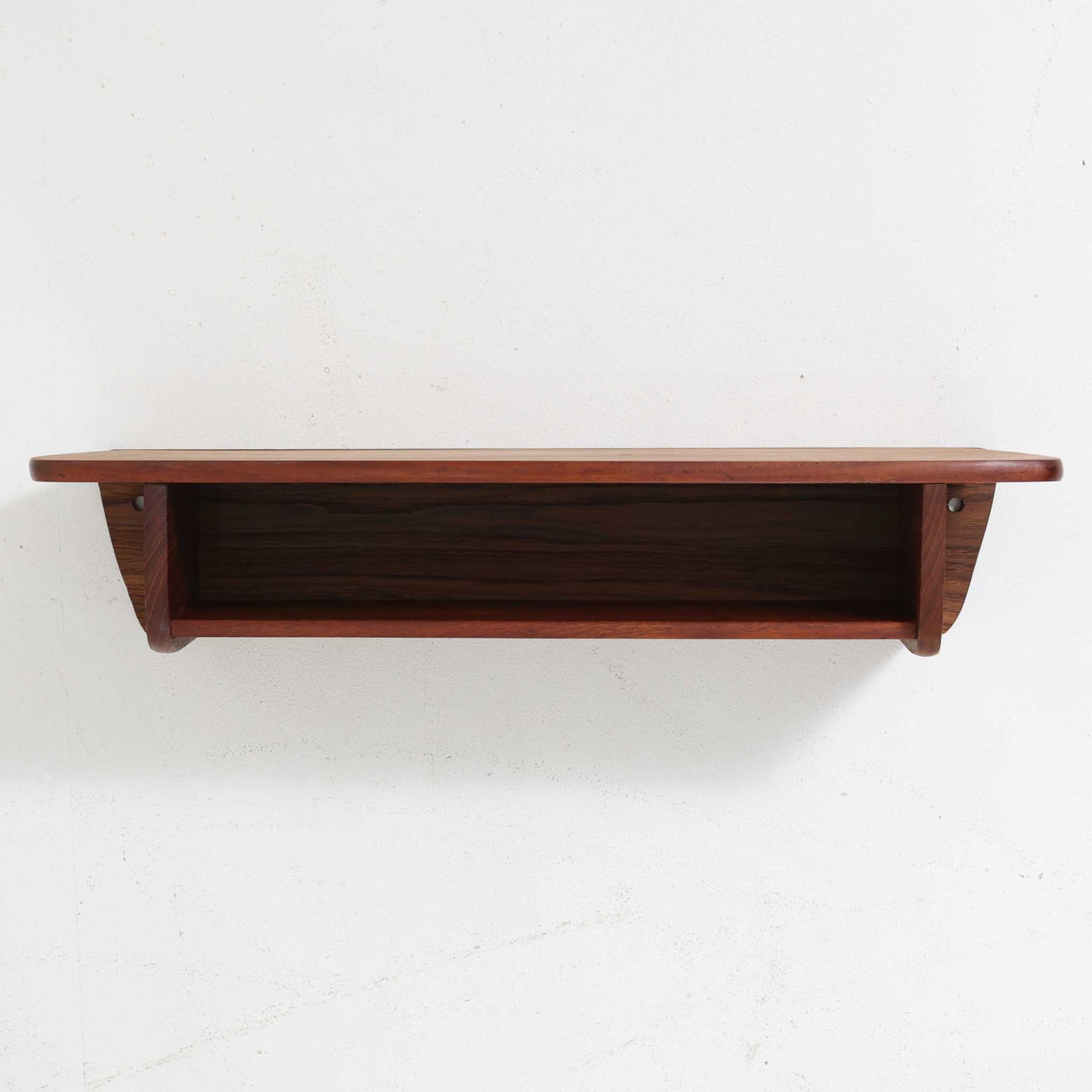 デンマーク製ウォールシェルフです。上質なチーク無垢材を使用し、滑らかなカーブを描く縁取りと丸みのあるフォルムが北欧家具らしい柔らかさを感じさせます。奥行きを抑えたコンパクトなサイズで、玄関や寝室、リビングのちょっとしたスペースにも取り付けやすい設計です。経年により深みを増したチーク材の美しい色合いが、壁面を上品に演出します。