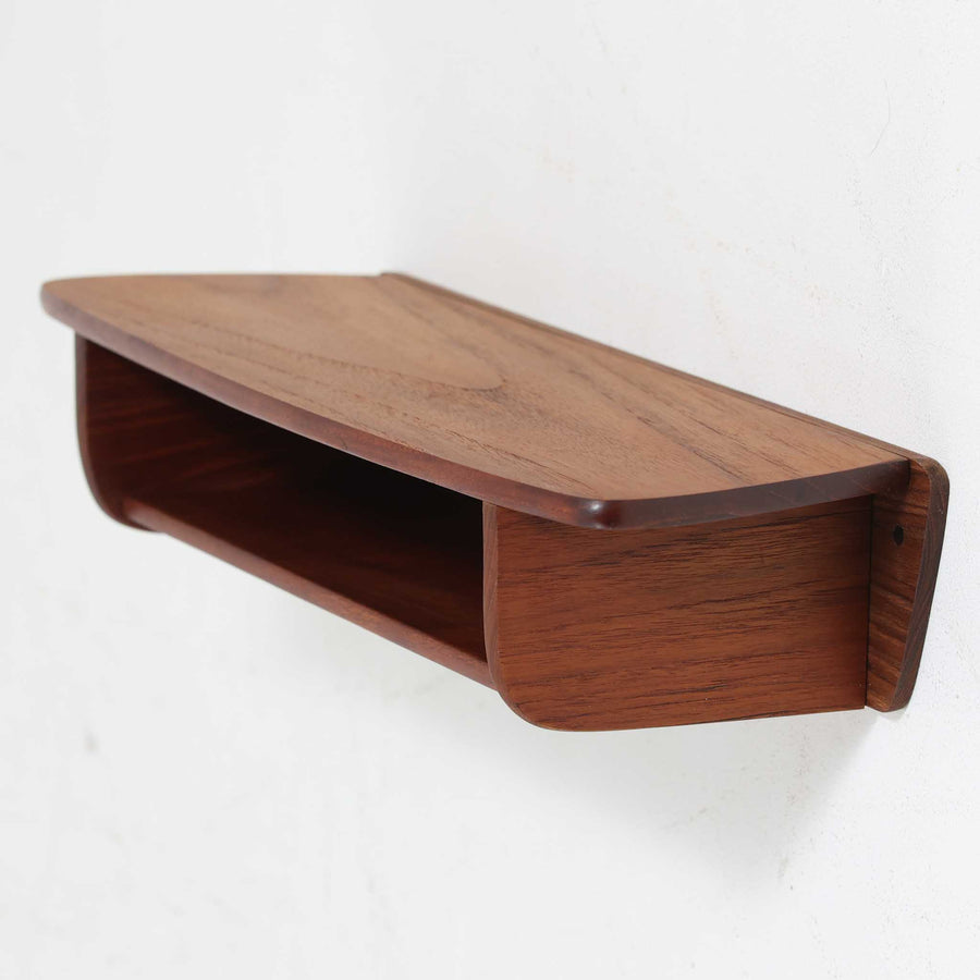 デンマーク製ウォールシェルフです。上質なチーク無垢材を使用し、滑らかなカーブを描く縁取りと丸みのあるフォルムが北欧家具らしい柔らかさを感じさせます。奥行きを抑えたコンパクトなサイズで、玄関や寝室、リビングのちょっとしたスペースにも取り付けやすい設計です。経年により深みを増したチーク材の美しい色合いが、壁面を上品に演出します。